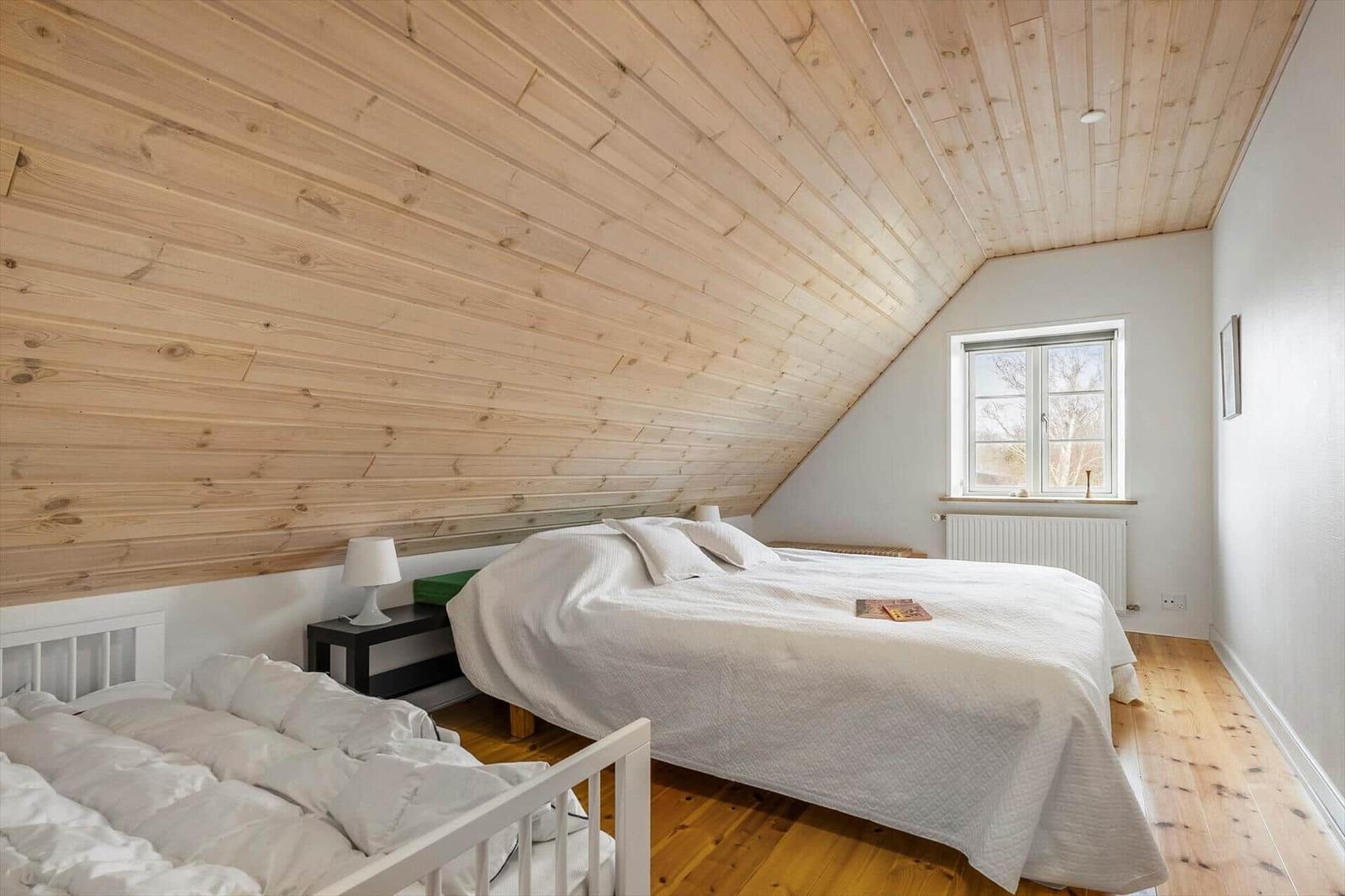Schlafzimmer mit Holzdecke, Bett und Fenster. Holzfußboden und Nachttisch.