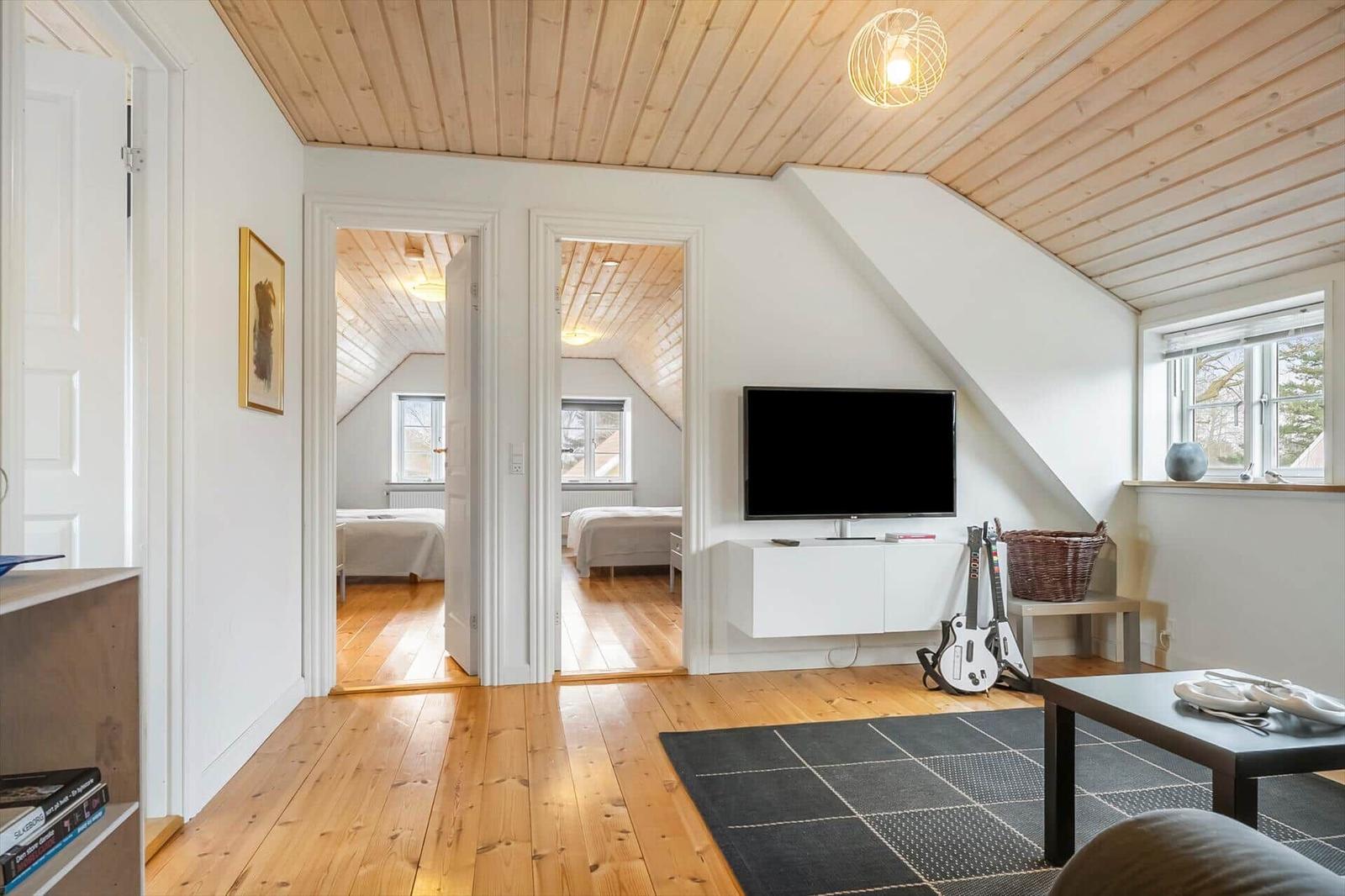 Wohnbereich mit Fernseher und Blick in Schlafzimmer. Holzdecke und -boden.
