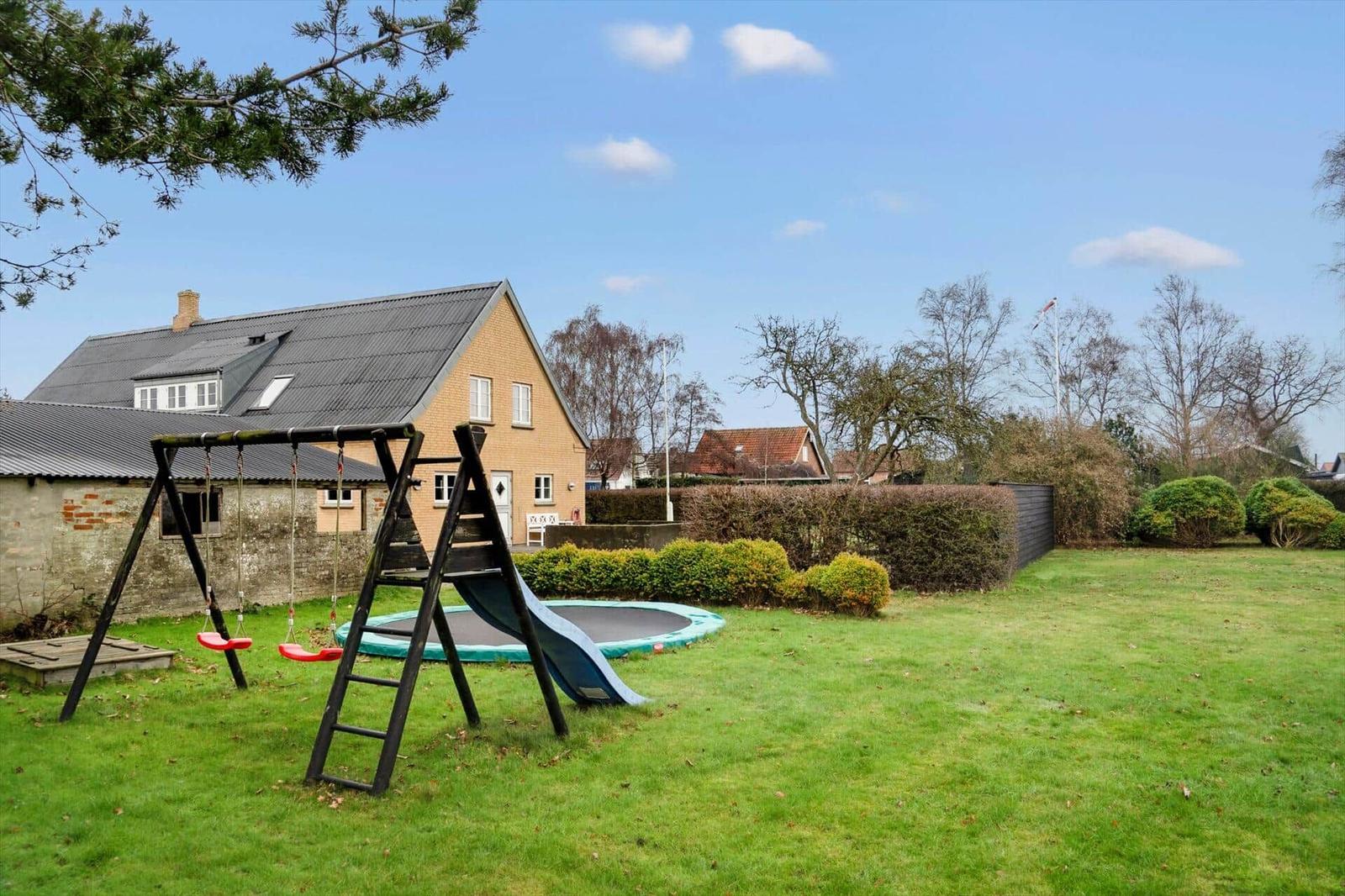 Haus mit Spielplatz, Trampolin und grünem Garten unter blauem Himmel.