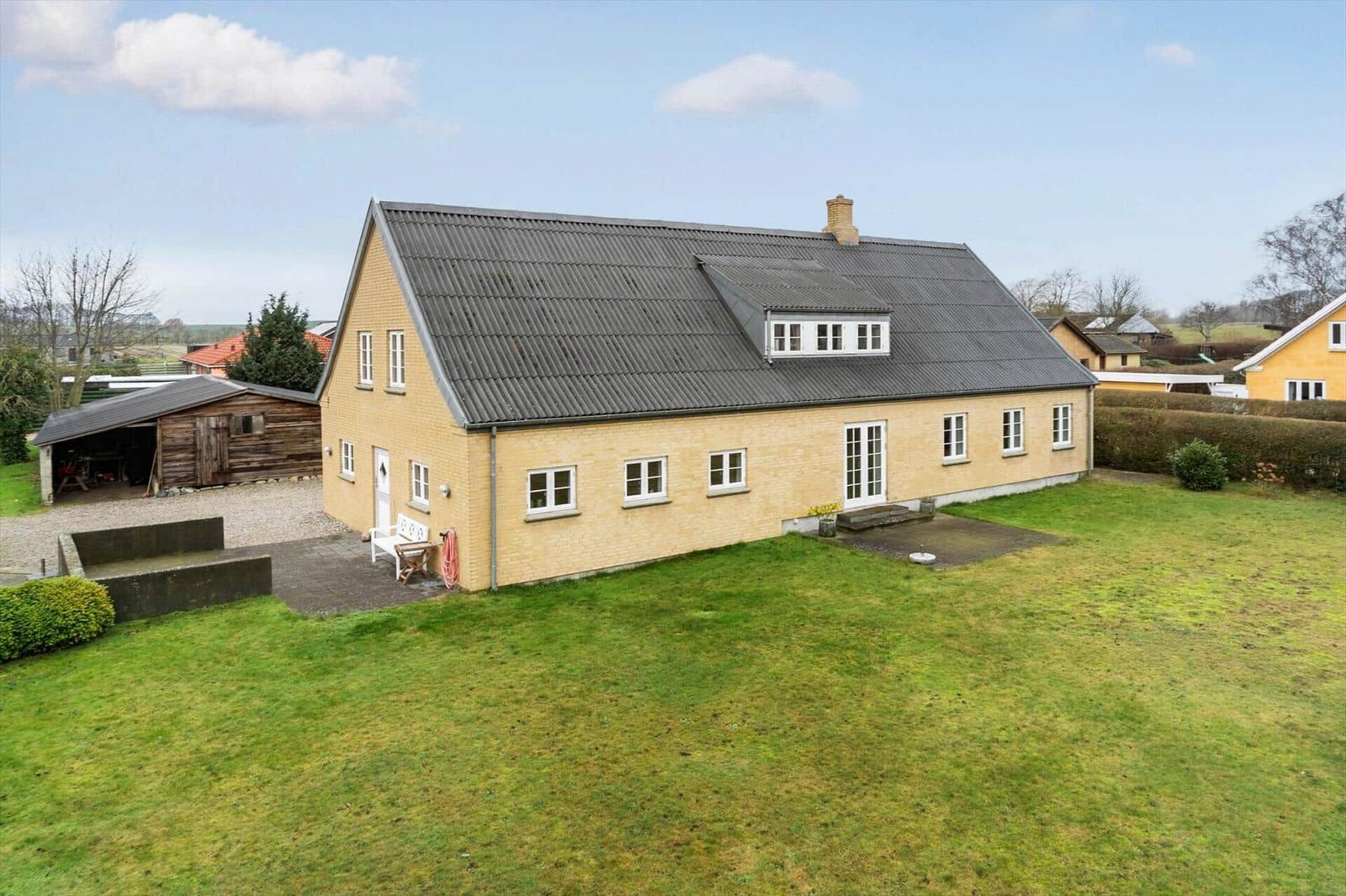 Ein gelbes Haus mit grauem Dach und grünem Garten. Neben einem Stall.