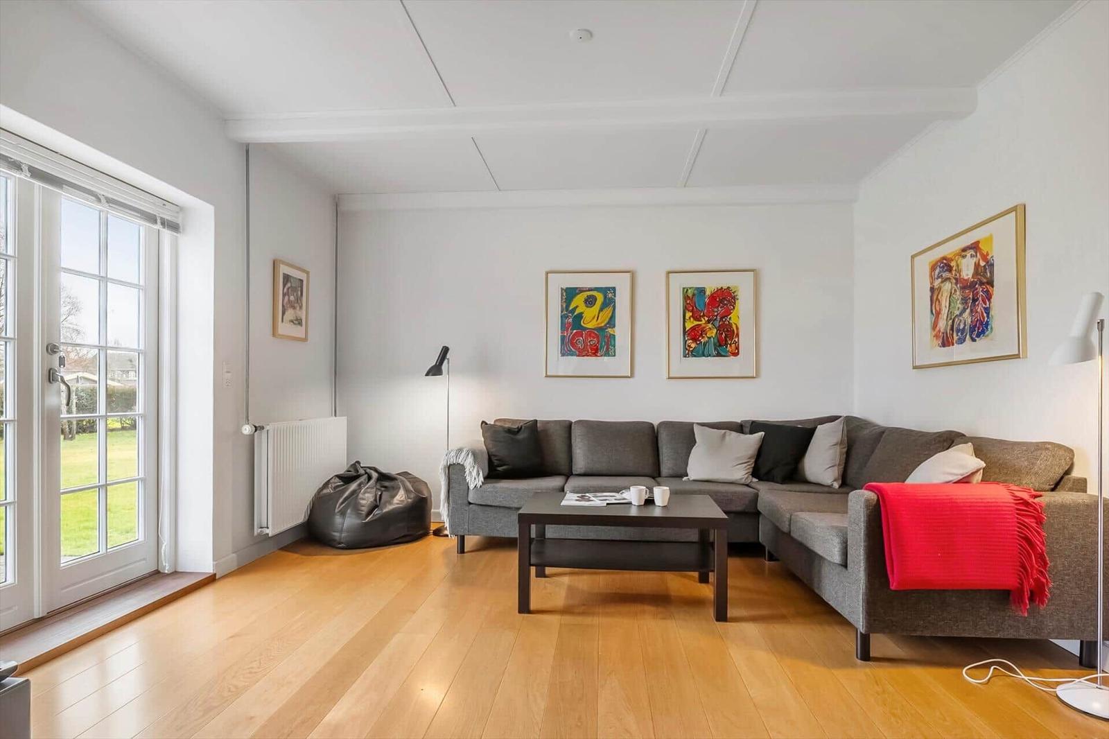 Wohnzimmer mit grauem Sofa, Holzboden und Fenster zur Grünfläche.