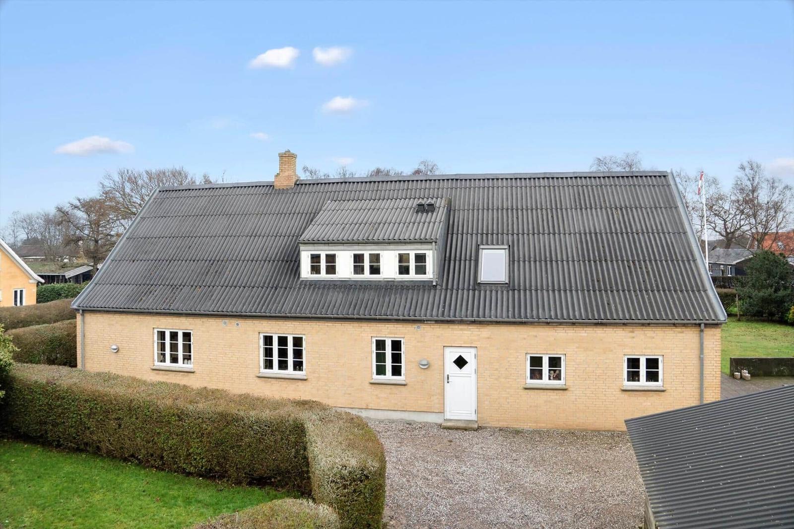 Ein hellgelbes Haus mit grauem Dach und weißer Tür.