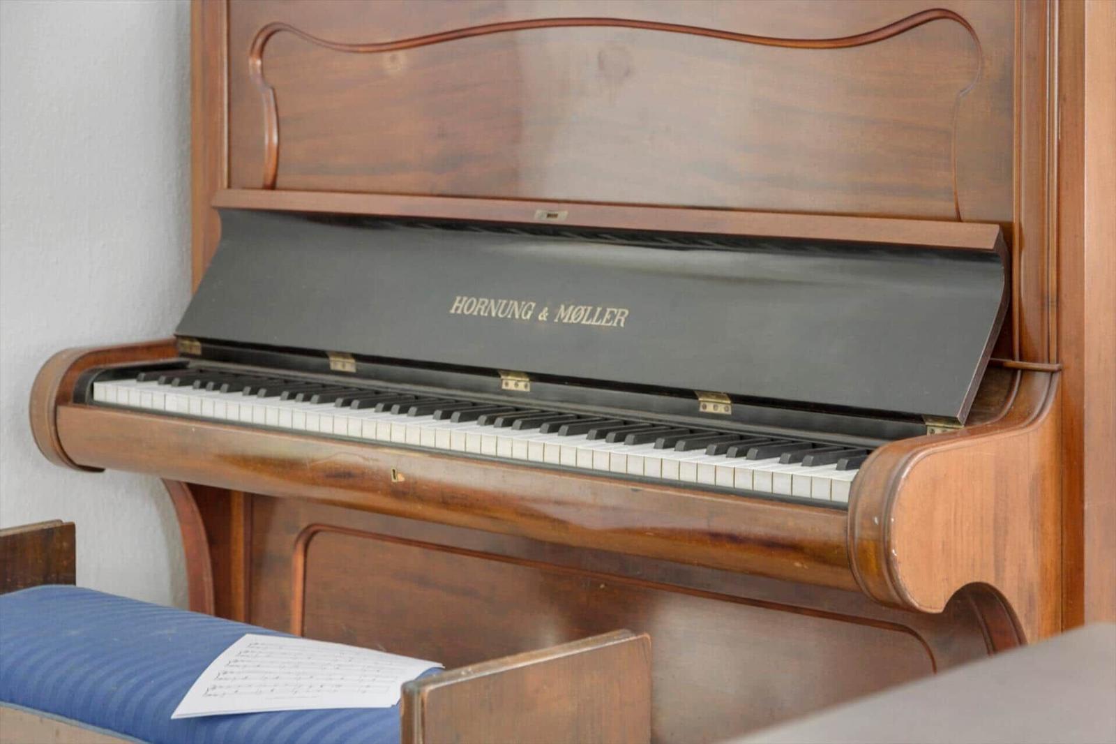 A piano with open lid and sheet music on the stool.
