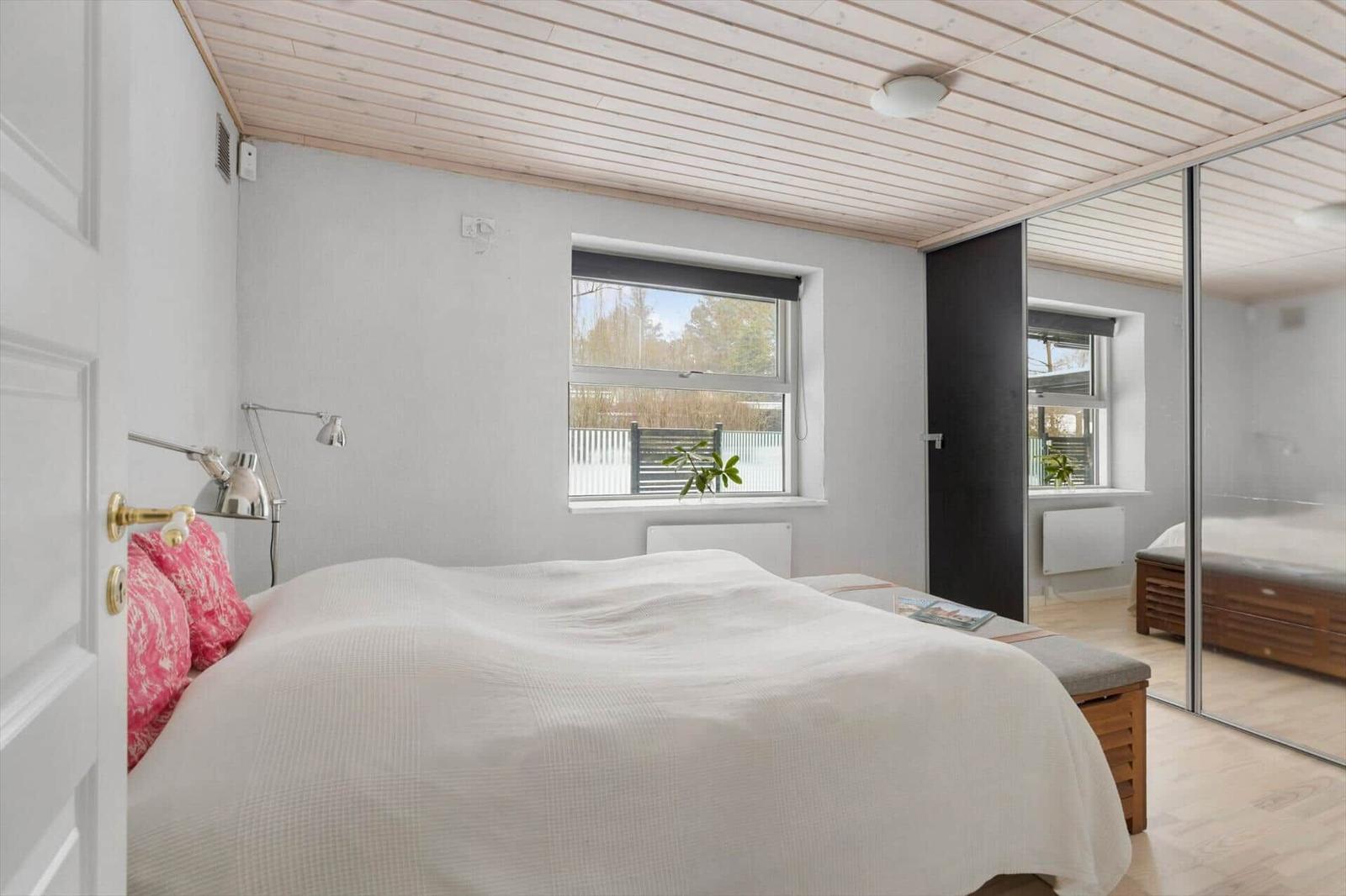 Bedroom with bed, window, and mirrored doors. Wooden ceiling and white walls.