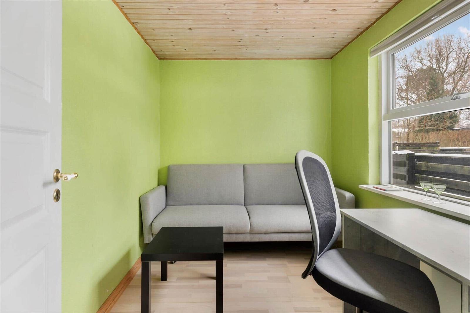 A room with green walls, sofa, desk, and window.