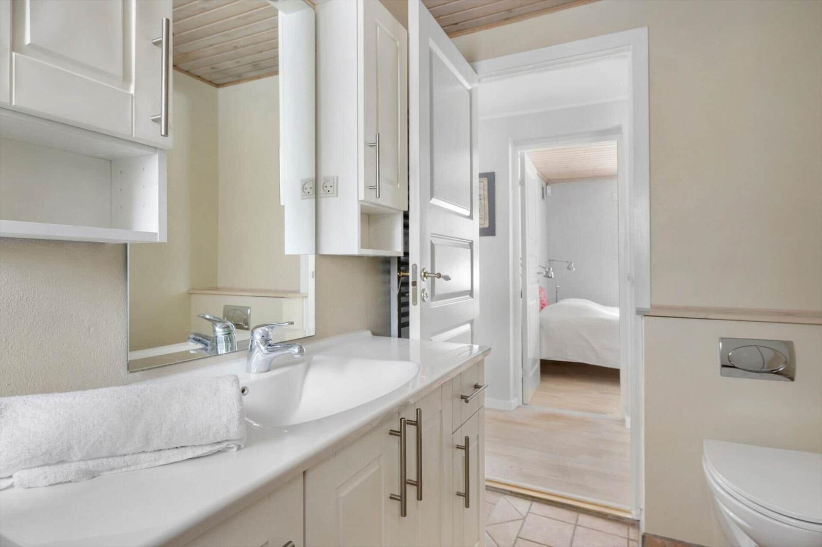 Bathroom with sink, mirror, and toilet. View into bedroom with bed.
