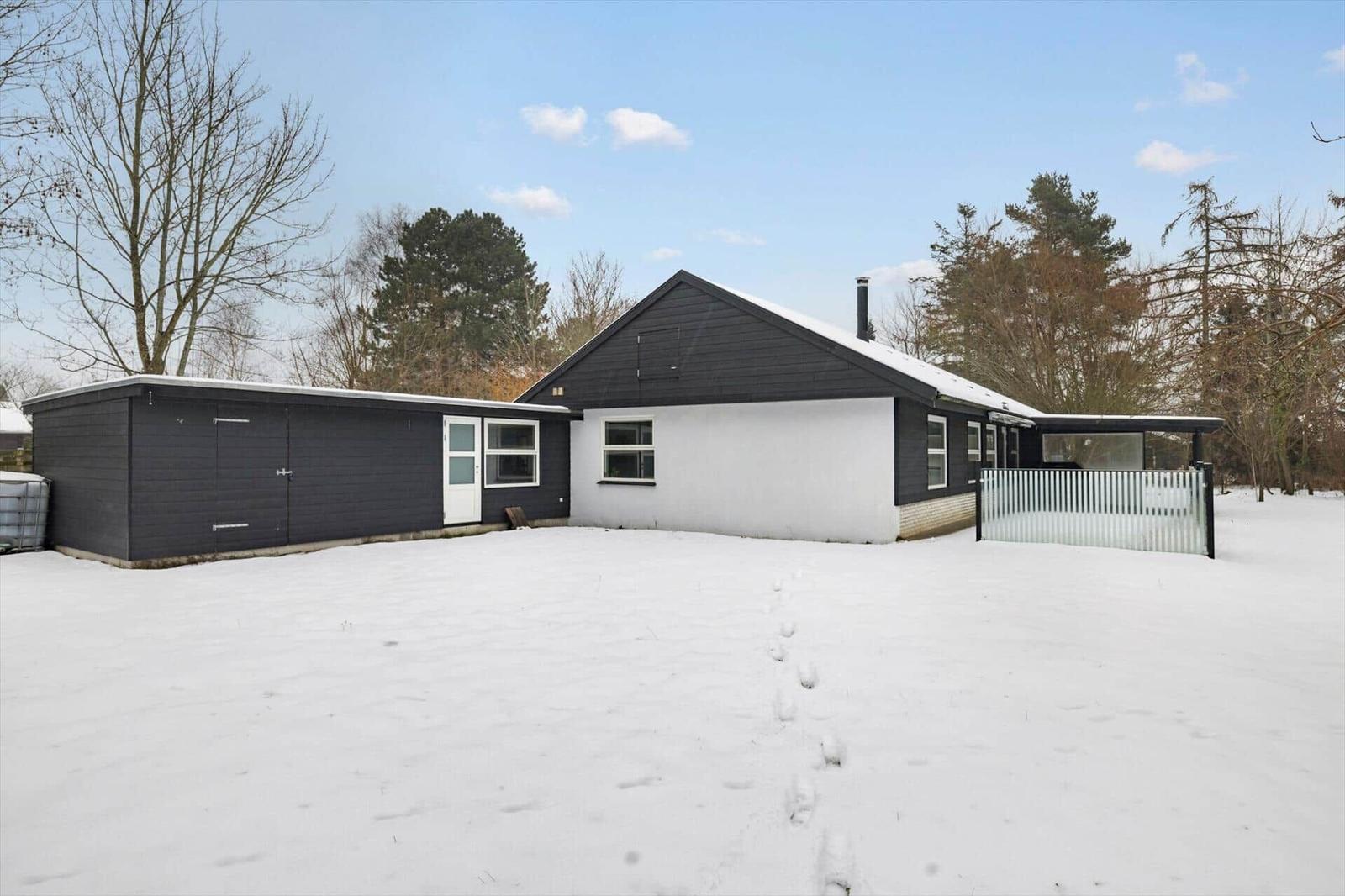 Black house with white facade, snow-covered garden and garage.