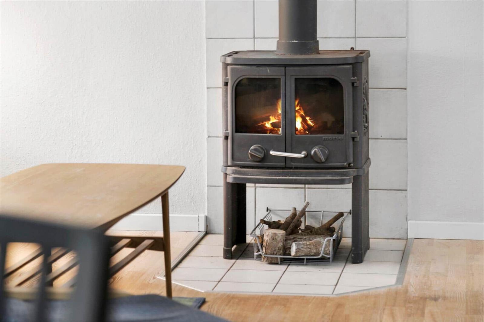 Wood stove with burning logs, wooden table, and tiled wall