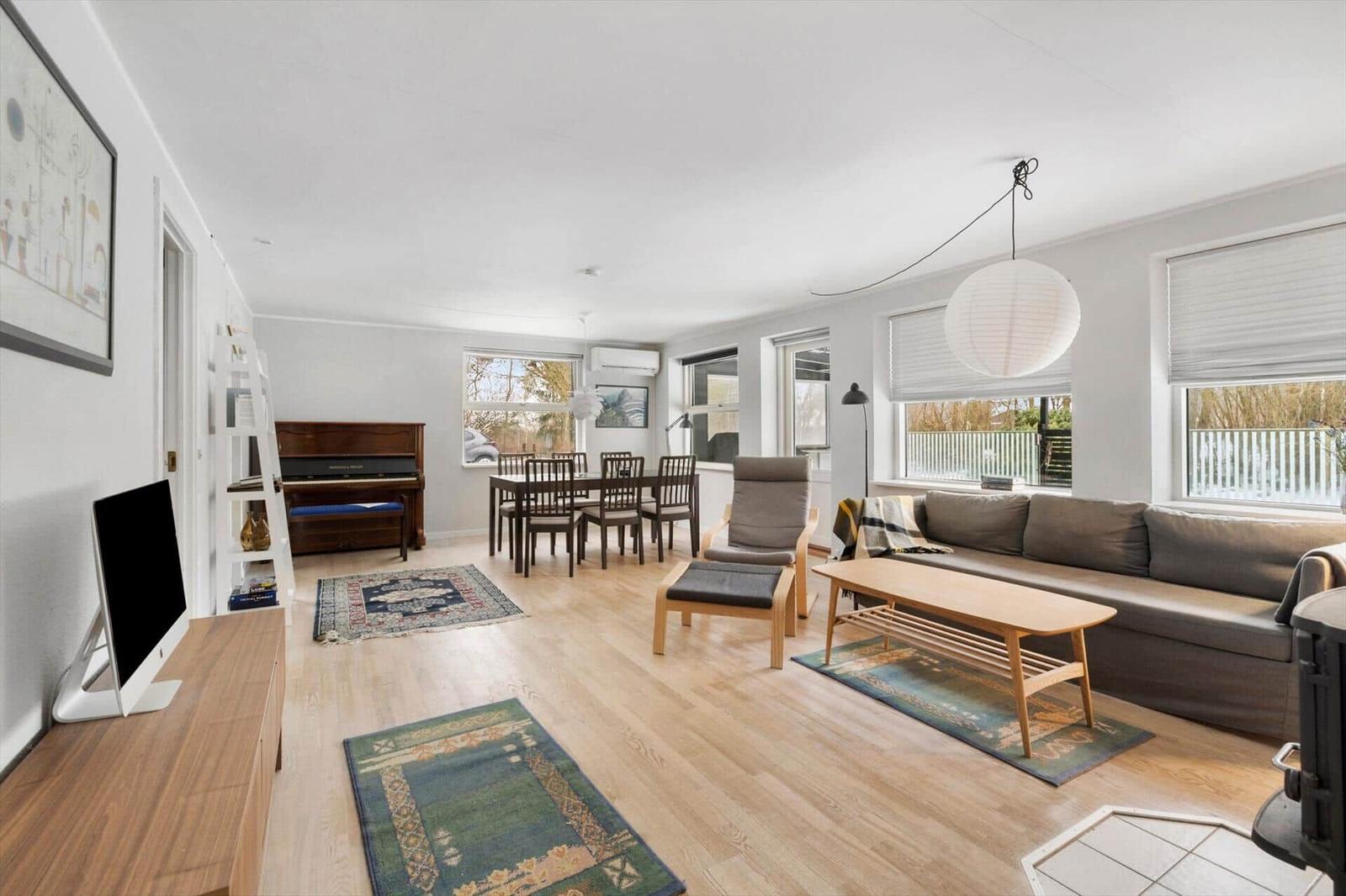 Living and dining area with sofa, table, piano, and windows.