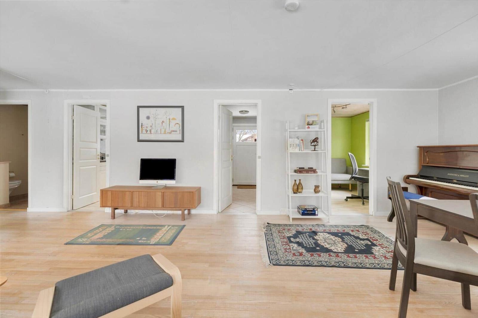Living room with hardwood floor, TV, hallway, and view into home office with piano.
