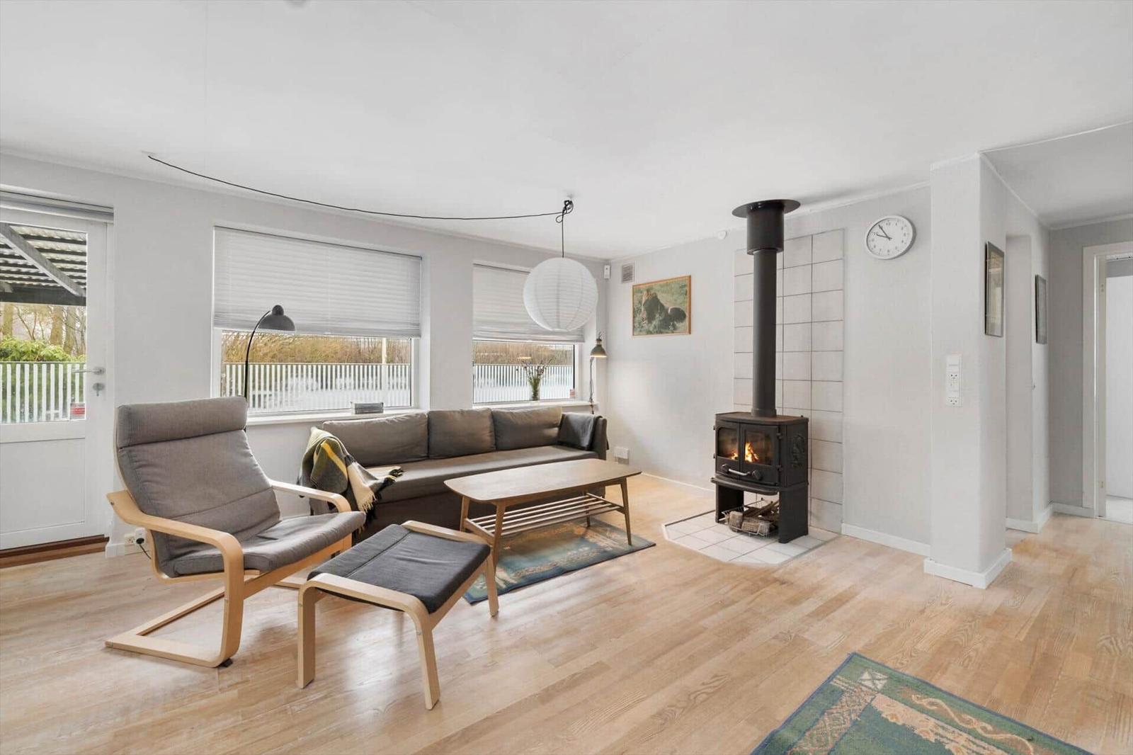Living room with sofa, armchair, stove, and wooden floor.
