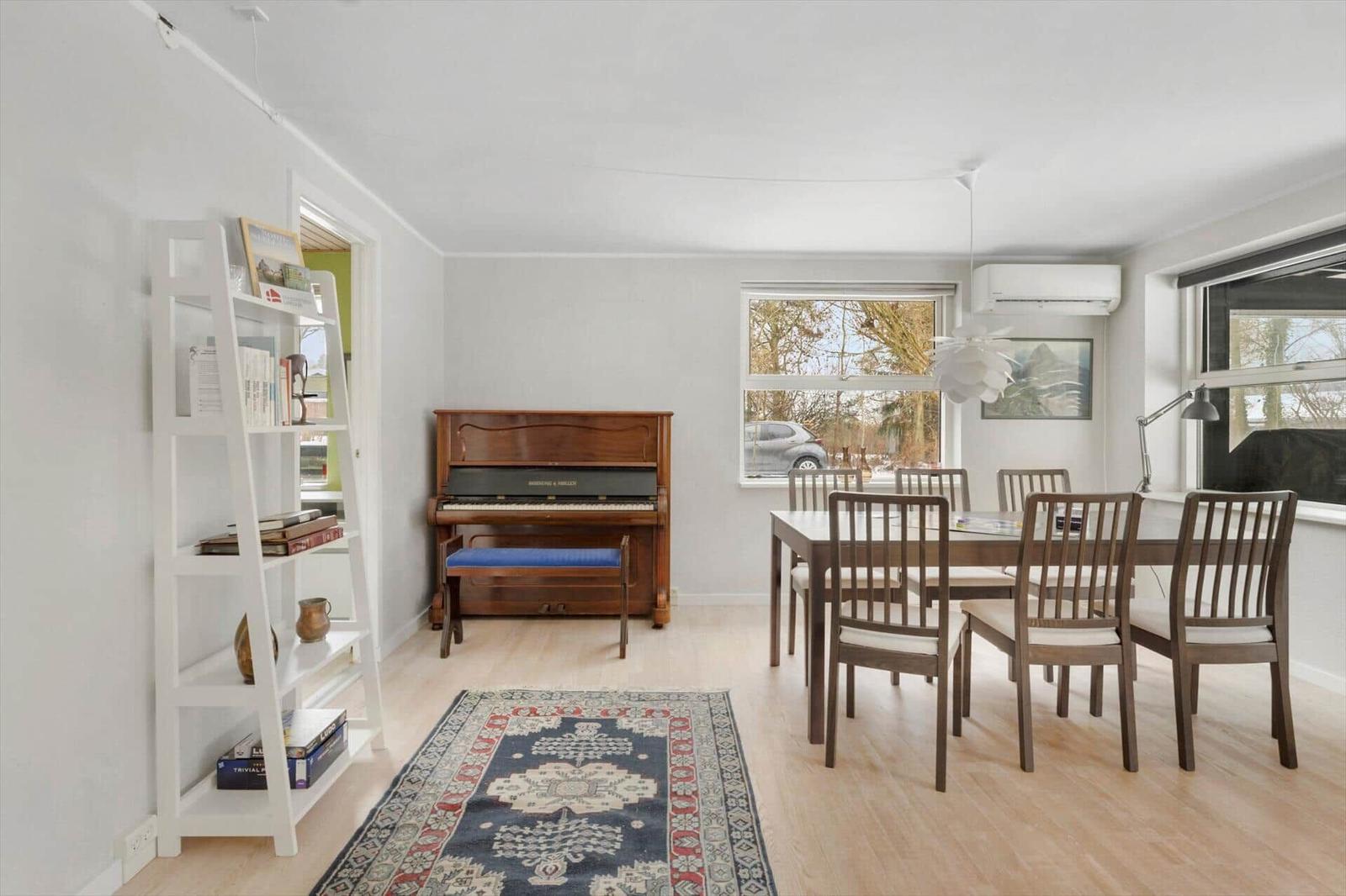 A room with dining table, chairs, runner rug, and piano.