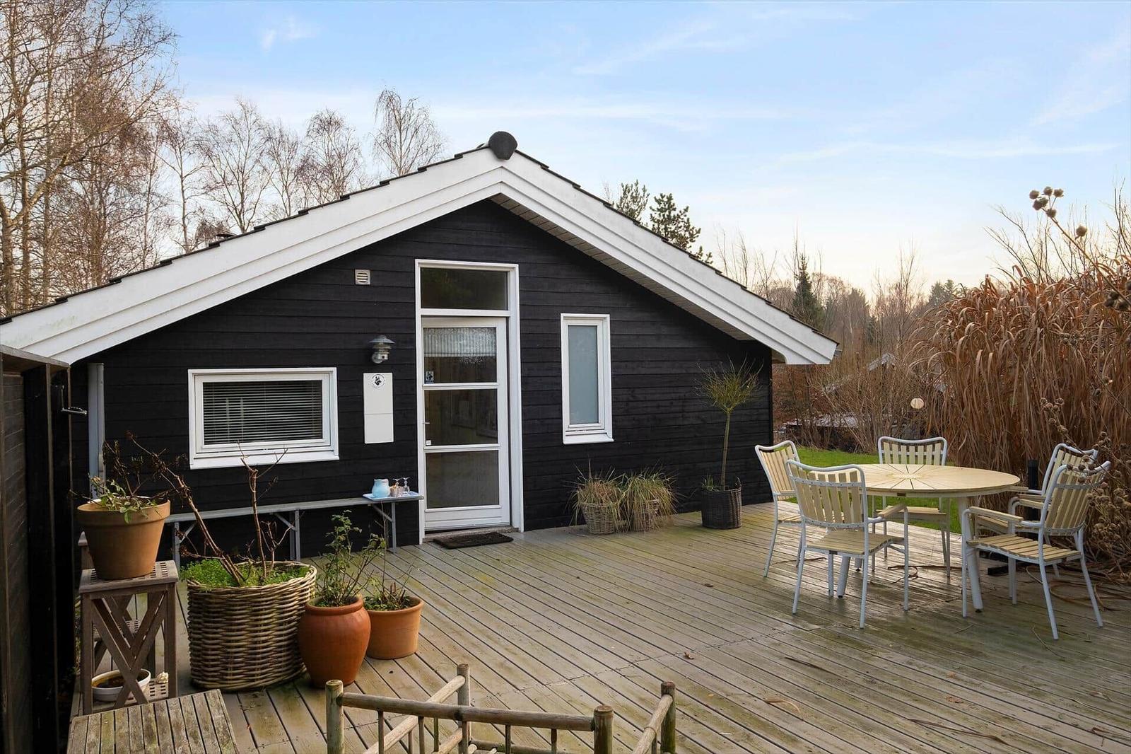Black wooden house with white roof and terrace with table and chairs.