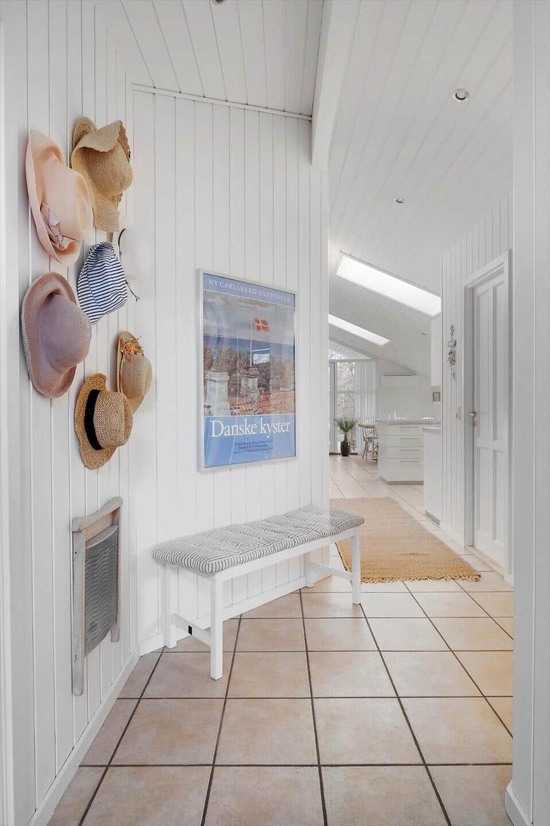 Entryway with bench, wall poster, and dried hats hanging on the wall.