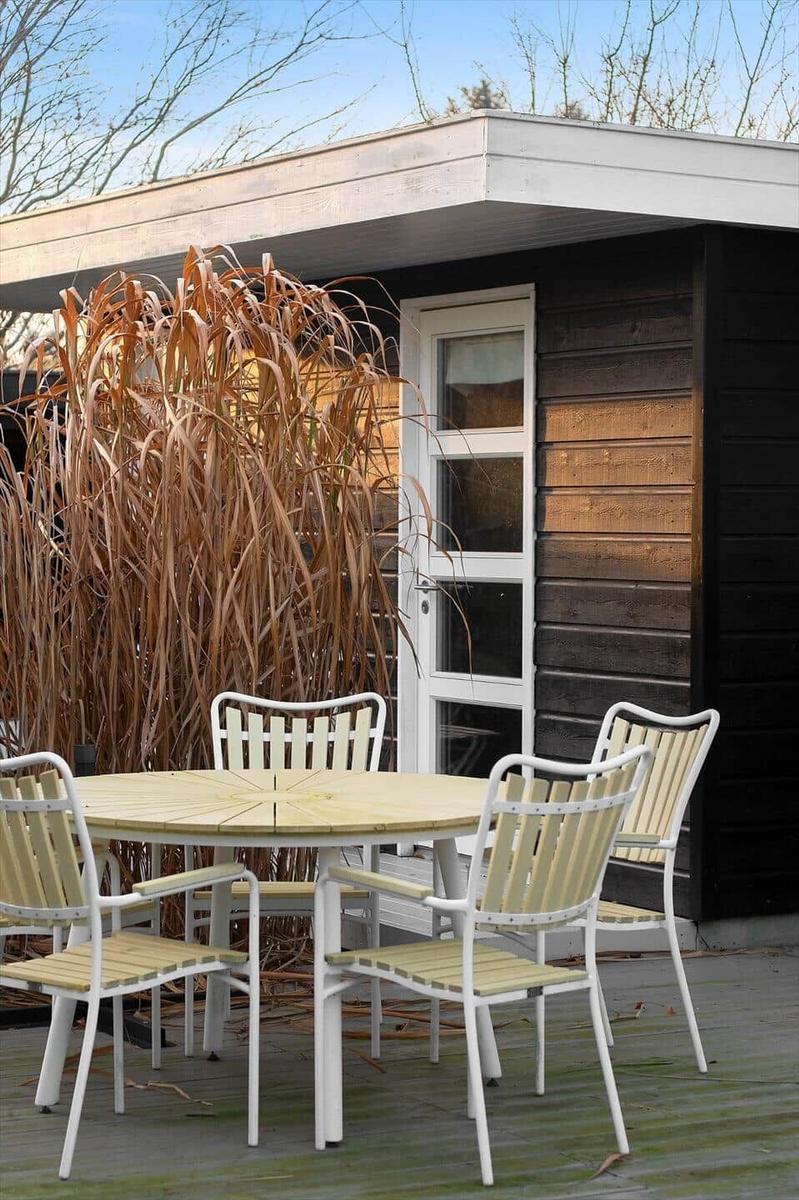 Deck with table and chairs in front of a wooden house with white windows.