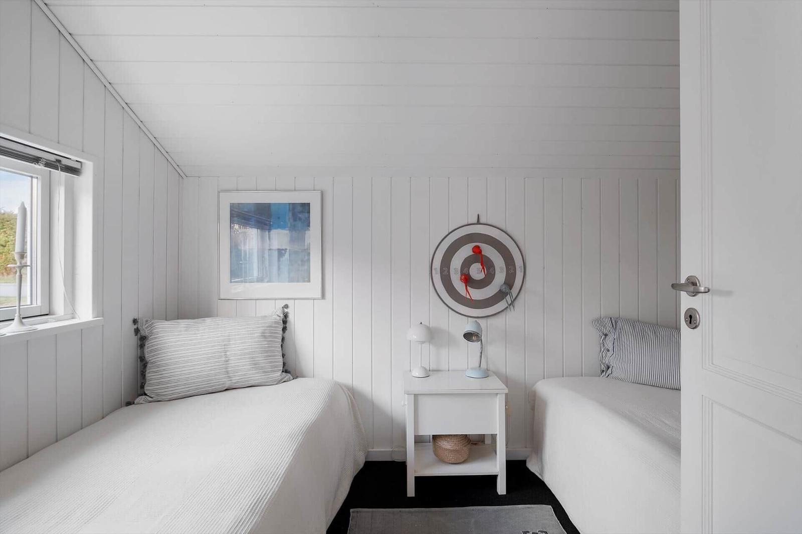 Two beds with striped pillows, nightstand with lamp and target on wall.
