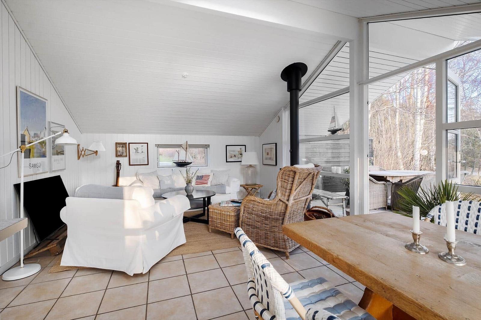 Living and dining area with wooden table, sofa, and seating. Large window front with view of outdoor area.