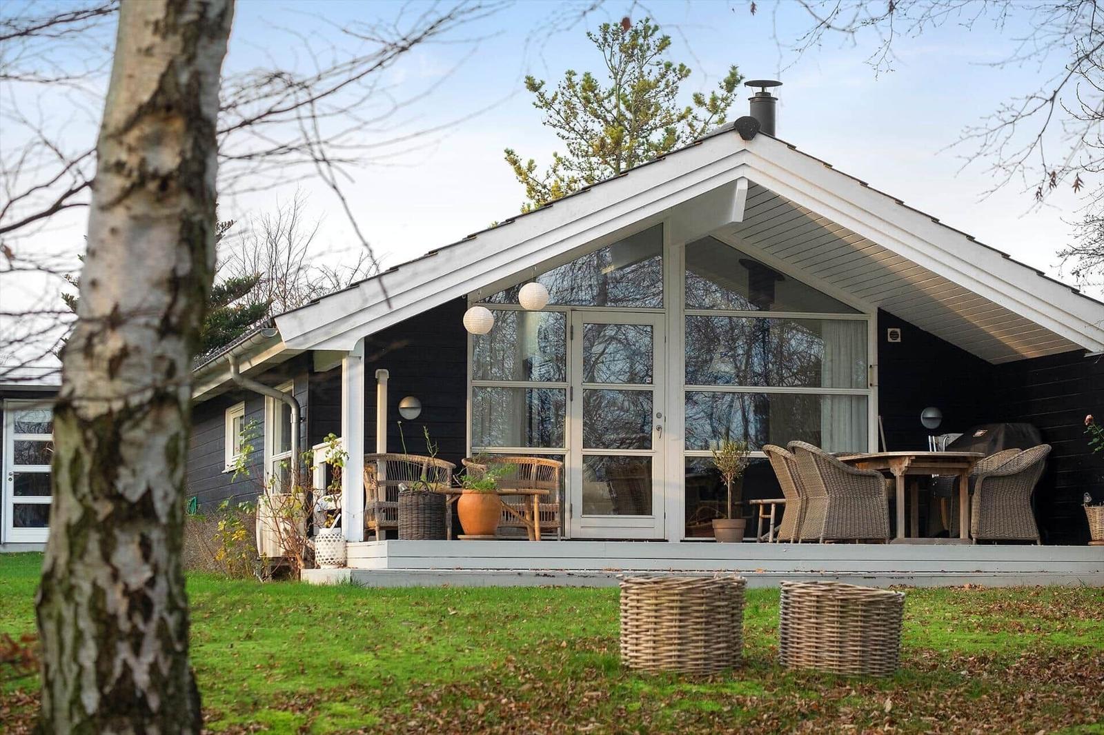 House with terrace, seating, and garden. Black facade and large windows.