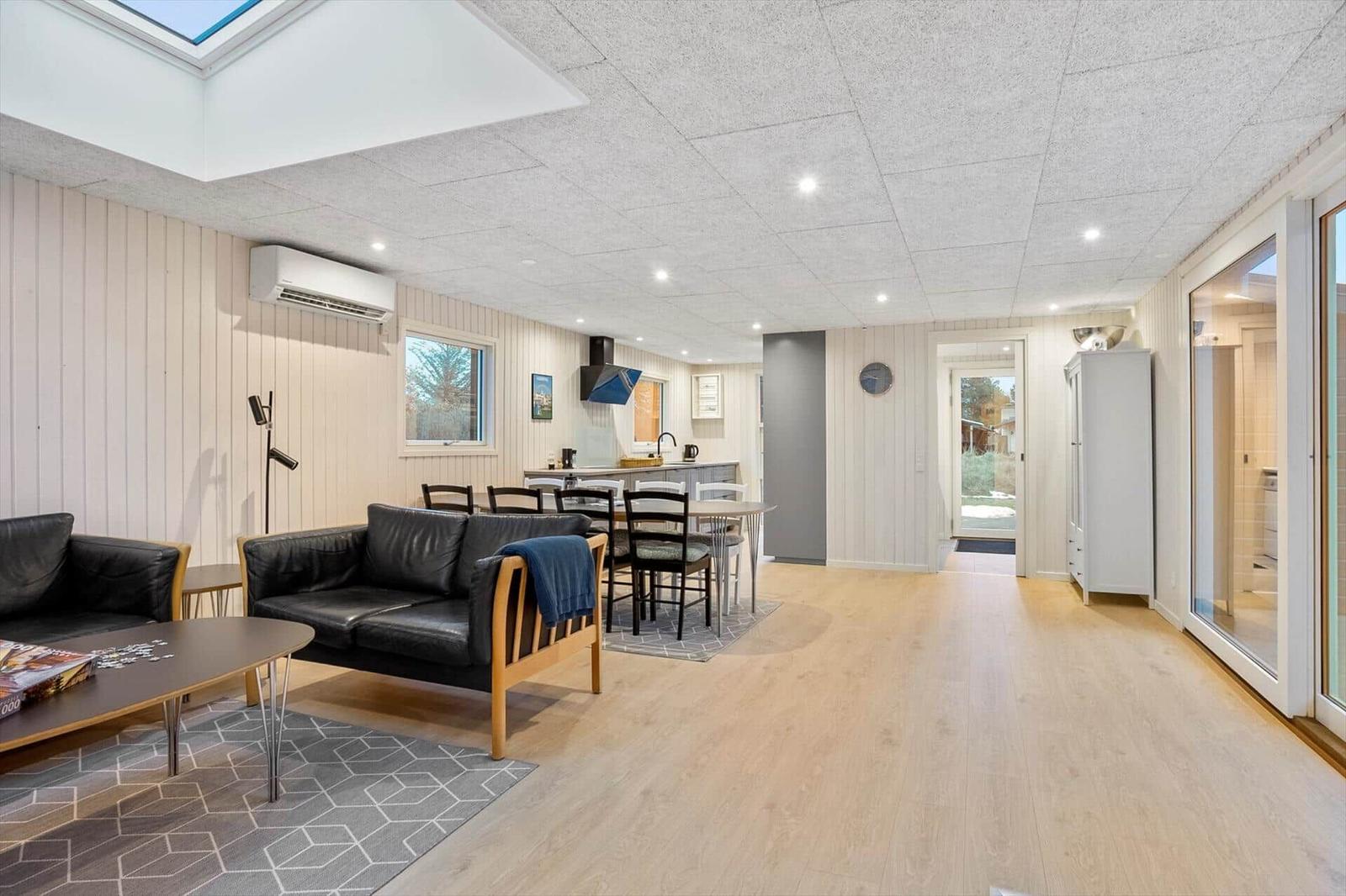 Living and dining area with kitchen, sofa, and table. Corridor to sauna.