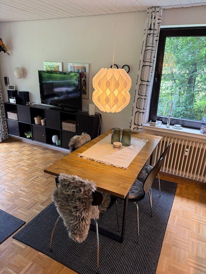 Essbereich mit Holztisch, Stühlen und Fensterblick auf Wald.