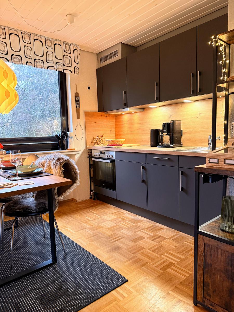 Küche mit Essbereich, Holzdielen und Fensterblick auf Bäume.