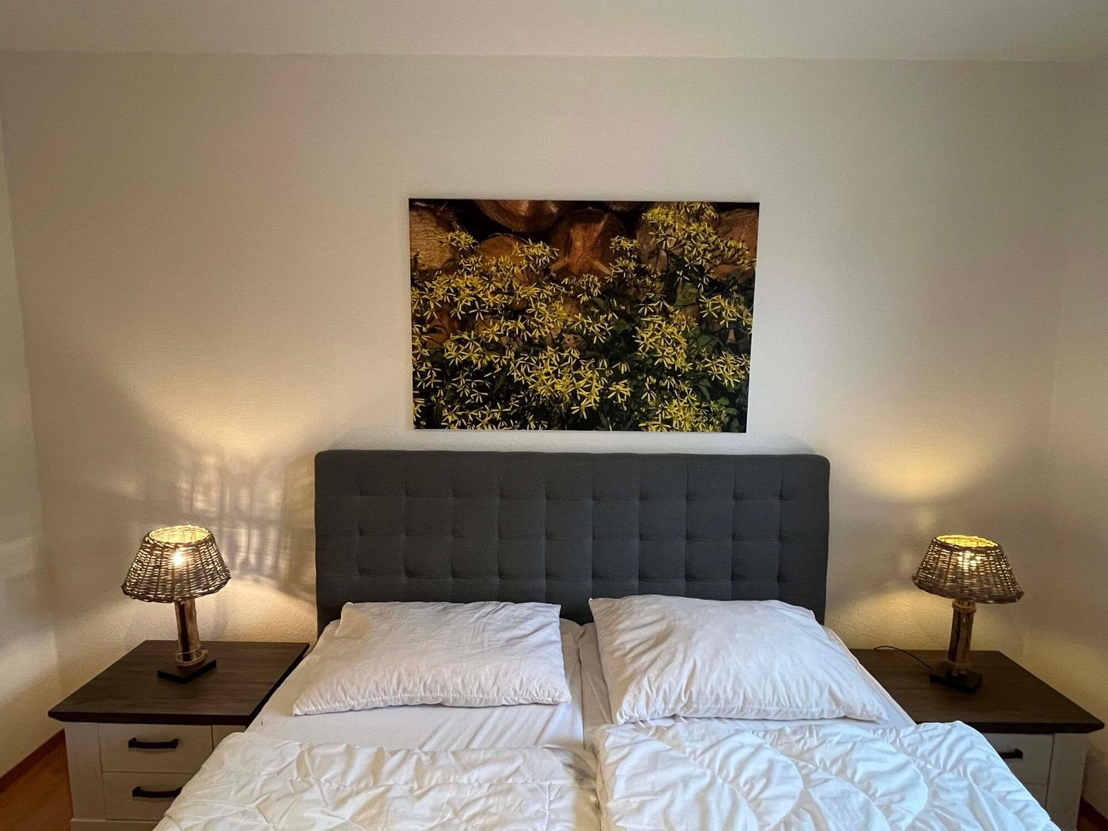 Schlafzimmer mit Bett, Nachttischen und Wandbild.