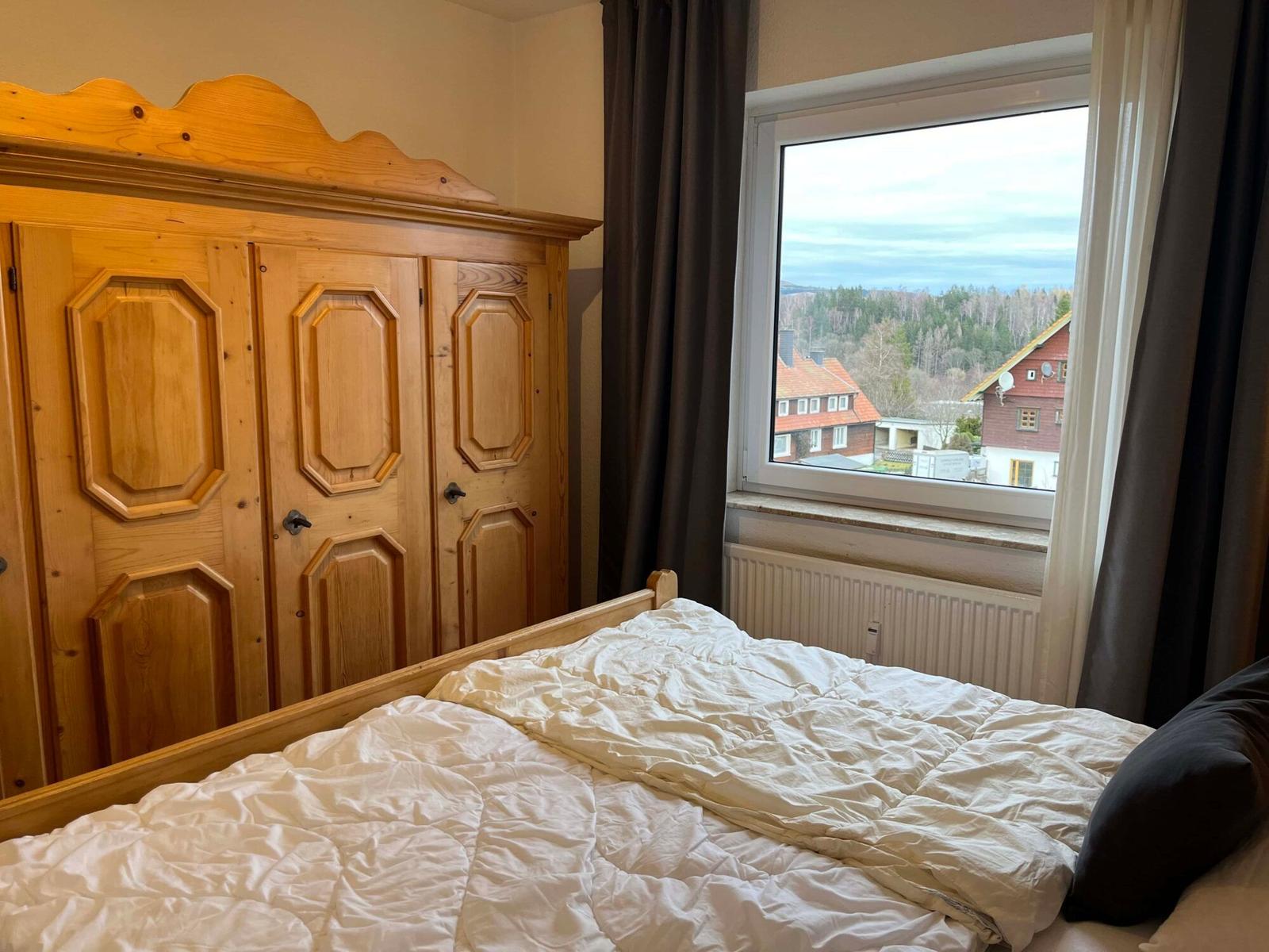 Schlafzimmer mit Holzschrank und Blick auf Wald und Häuser.
