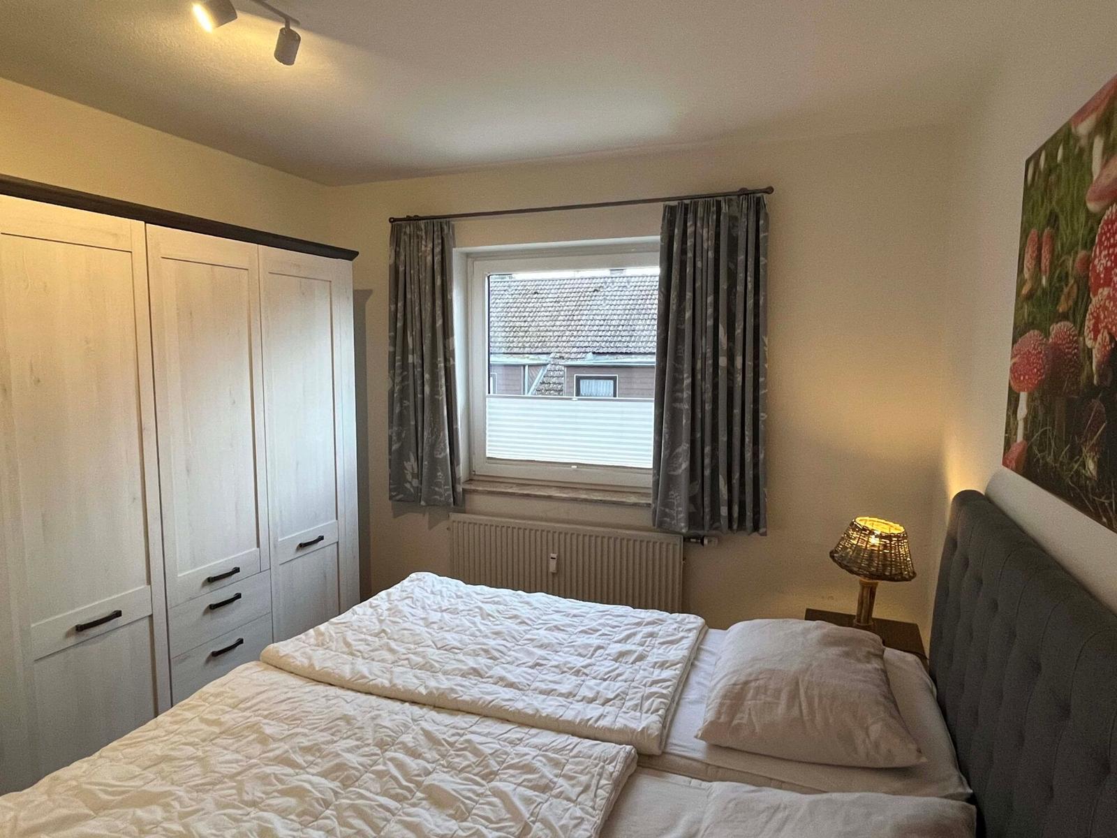 Schlafzimmer mit Doppelbett, Kleiderschrank und Fenster mit Vorhängen.