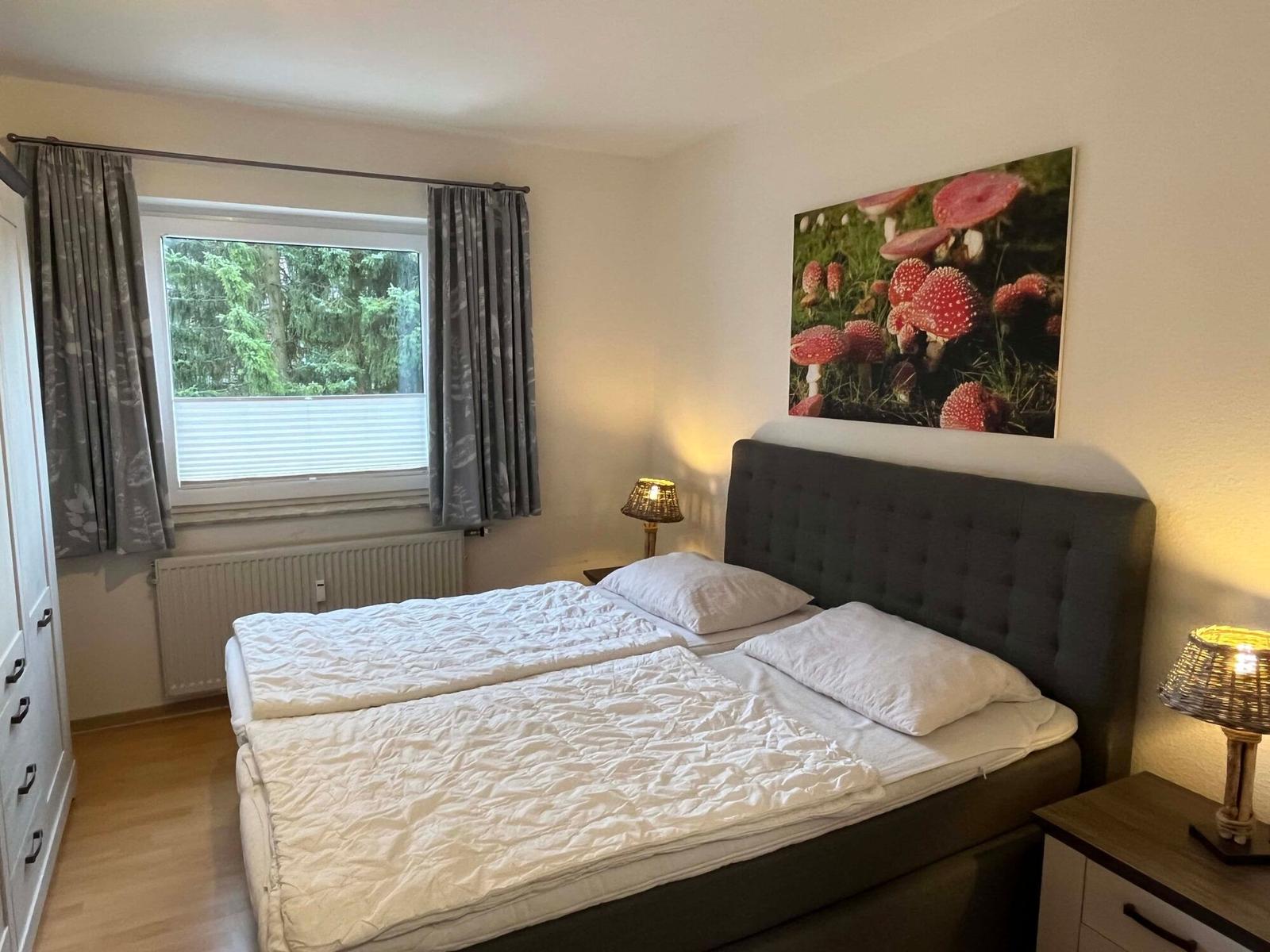 Schlafzimmer mit Doppelbett, Fenster und Wandbild mit Pilzen.