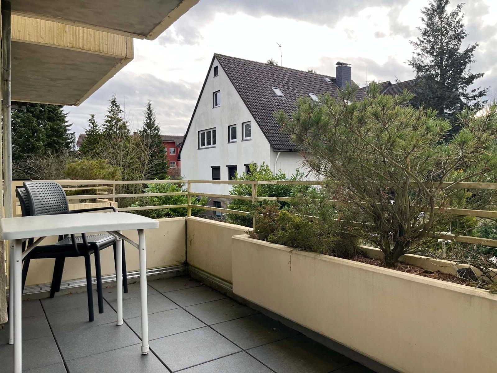 Balkon mit Tisch und Stühlen, Blick auf Wohnhaus und Bäume.