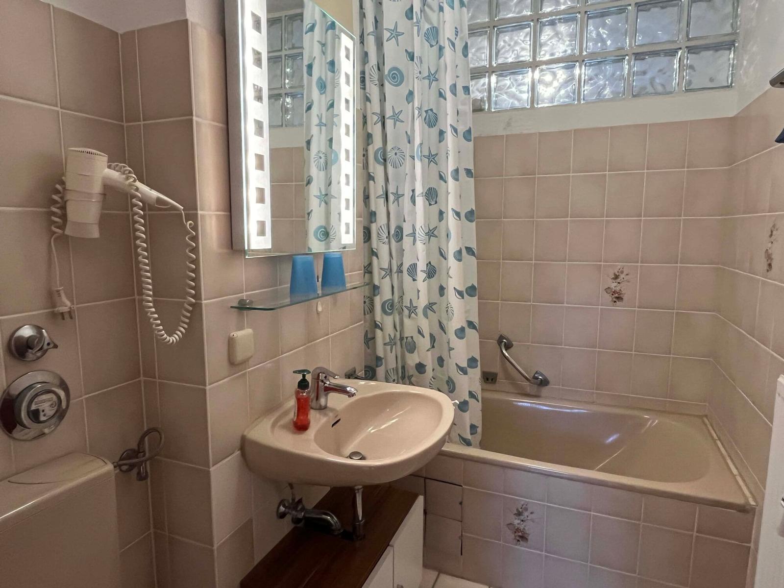 Badezimmer mit Badewanne, Spiegel und Duschvorhang mit Muster.