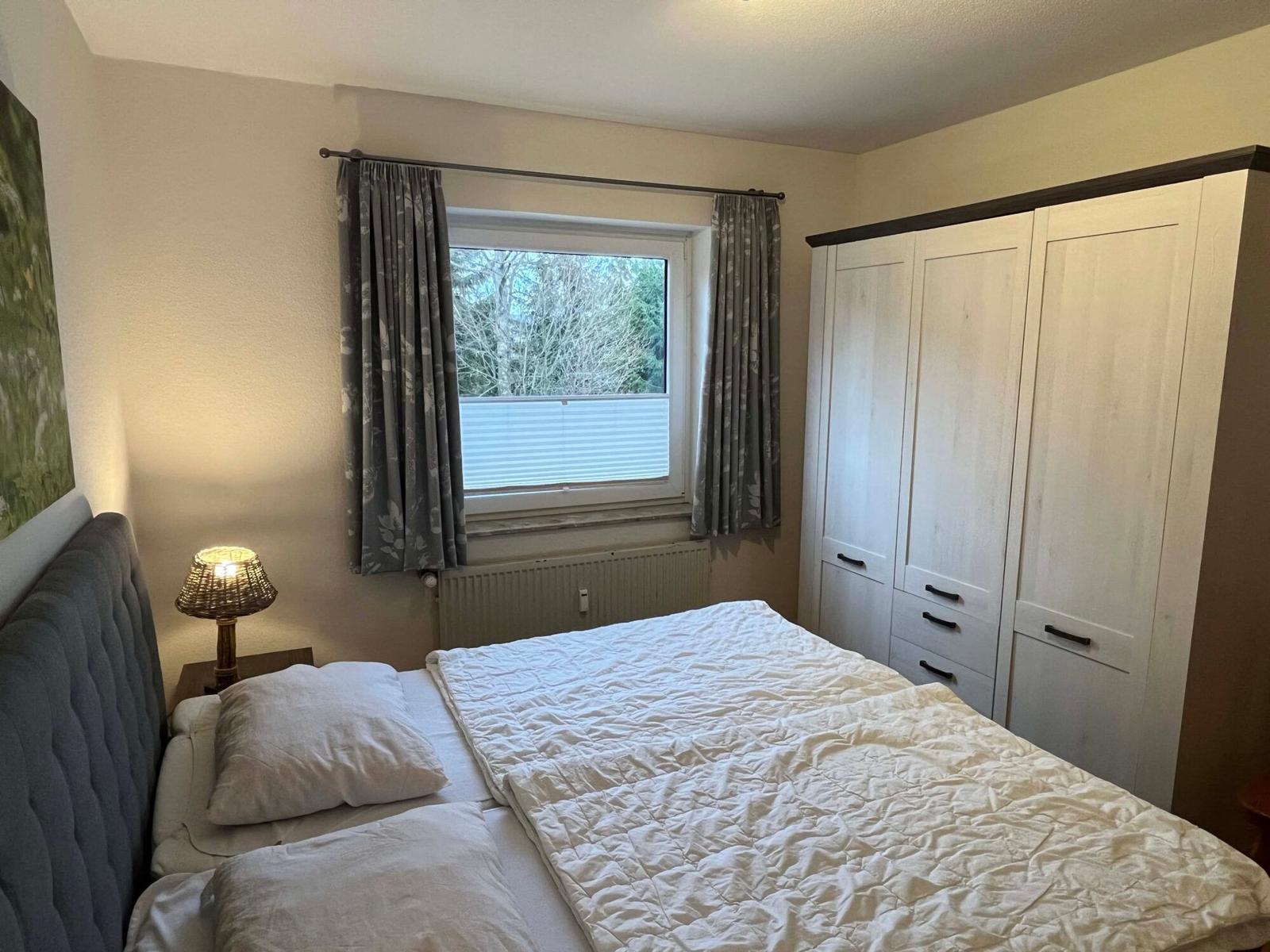 Schlafzimmer mit Bett, Kleiderschrank und Fenster mit Vorhängen.