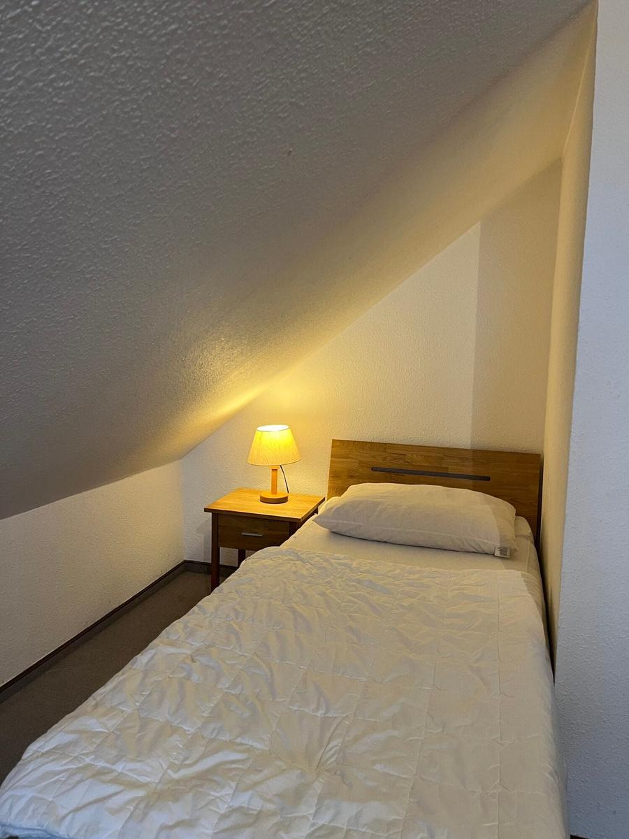 Ein Schlafzimmer mit Dachschrägen, Bett, Nachttisch und Lampe.