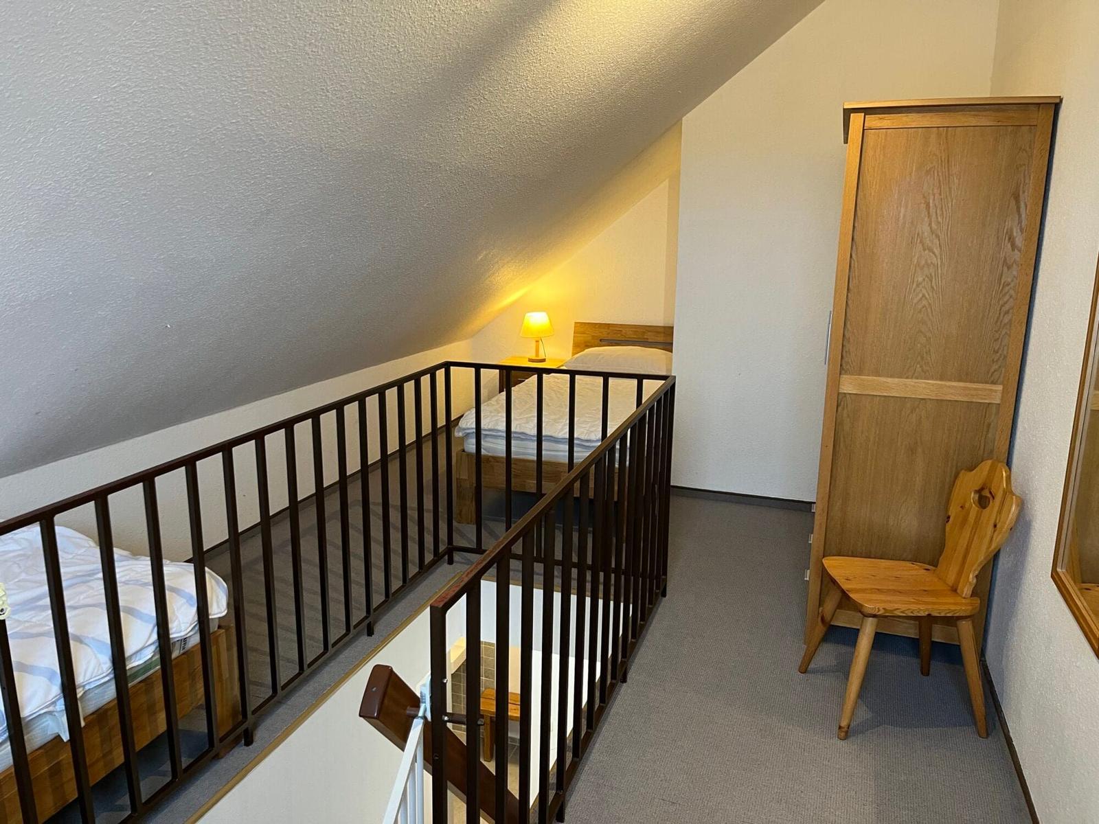 Zimmer mit Dachschrägen, Bett, Kleiderschrank und Stuhl.