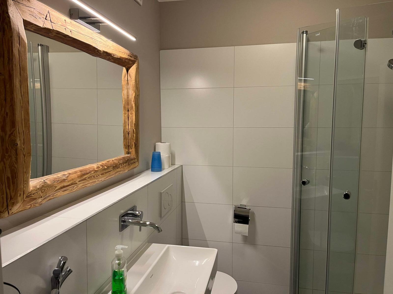 Bad mit Dusche, Waschbecken und Spiegel mit Holzrahmen