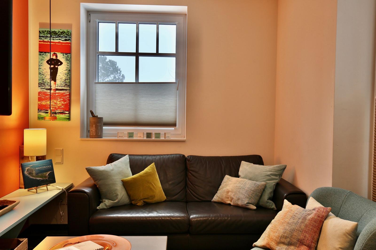 Schwarzes Ledersofa mit Kissen unter Fenster mit Jalousie.