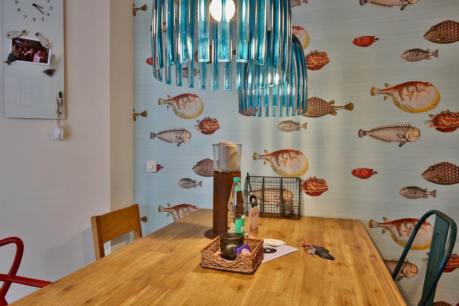 Esszimmer mit Fisch壁纸, Holztisch und blauem Hängelicht.