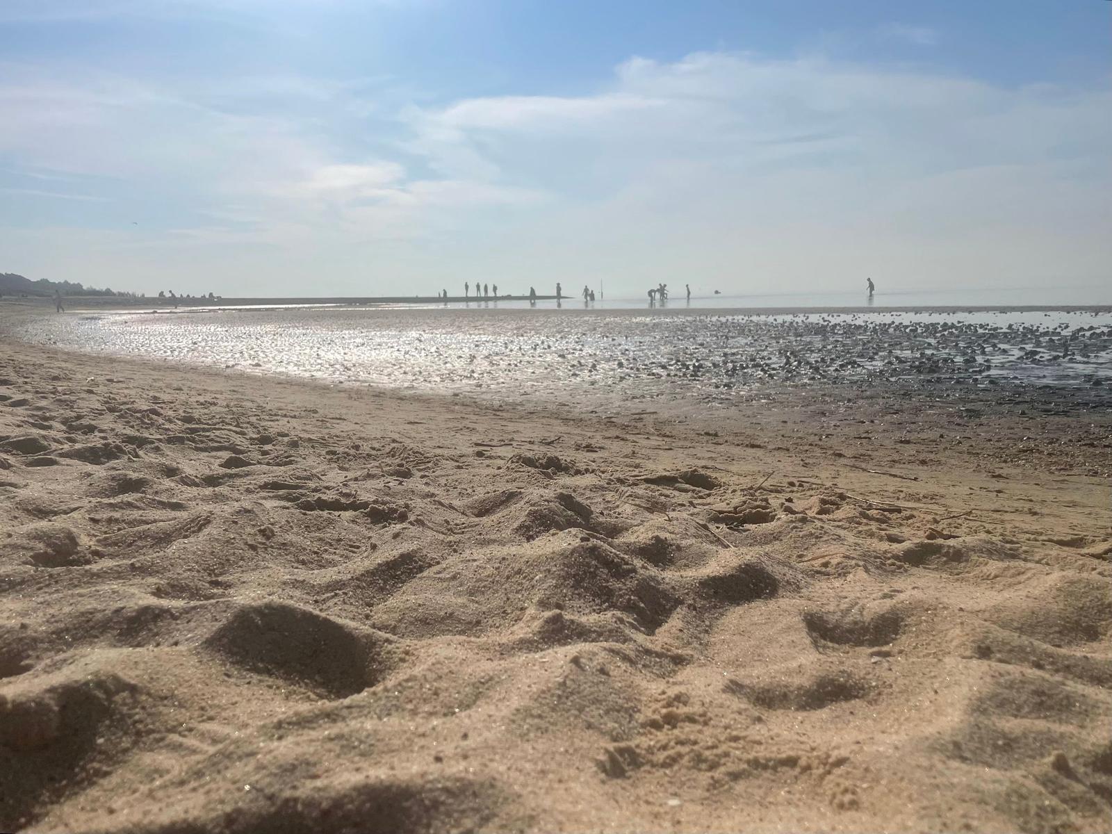 Beach with fine sand and people in the water at sunset.