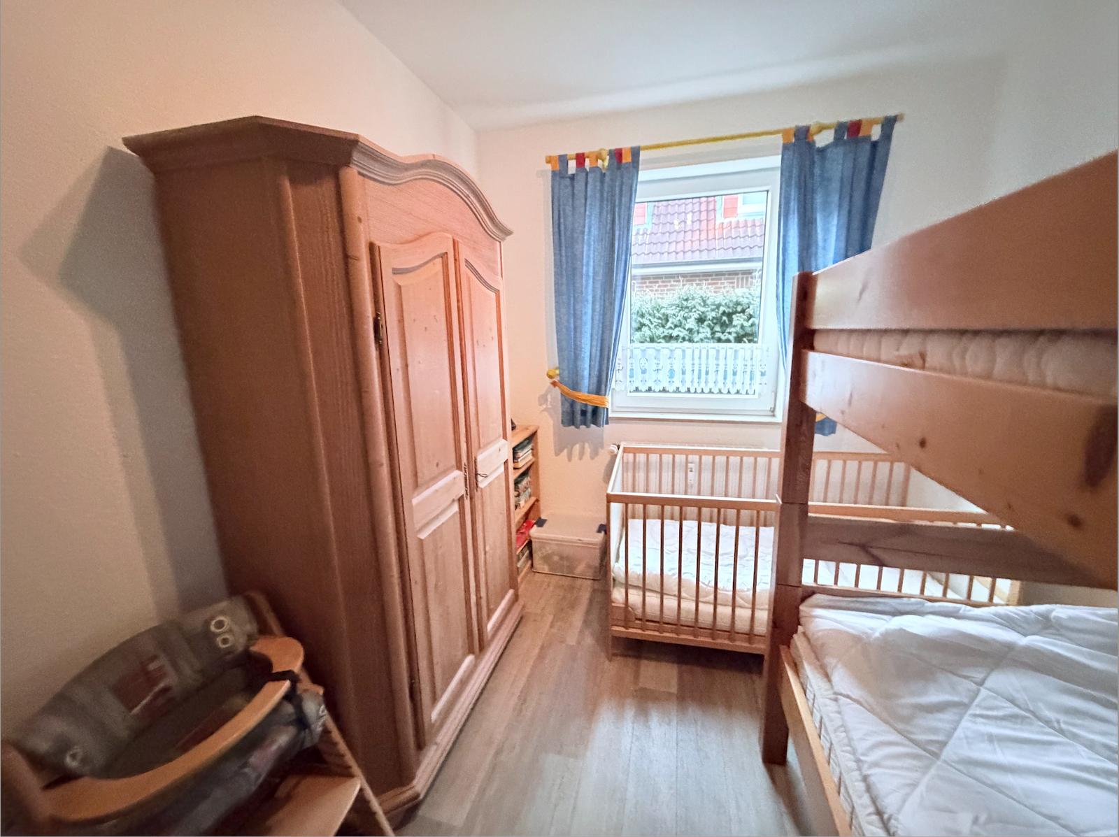 Room with crib, bunk bed, and wooden wardrobe. Window with blue curtains.
