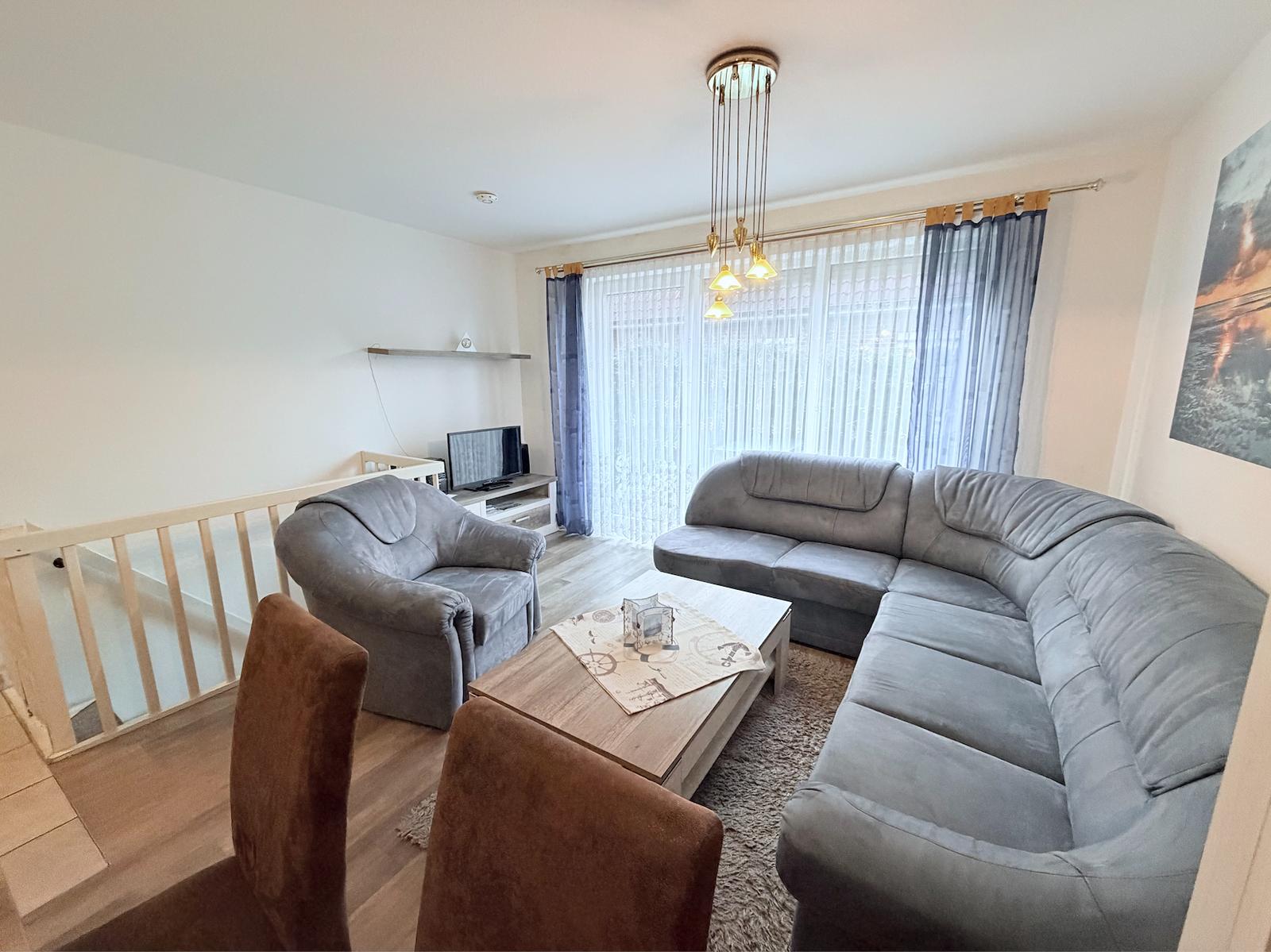 Living room with gray sofa, coffee table, and TV. Windows with curtains.