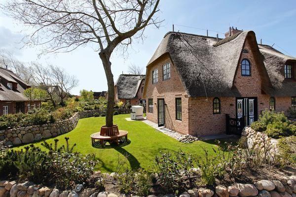 House with thatched roof and green garden. Wooden bench under tree.