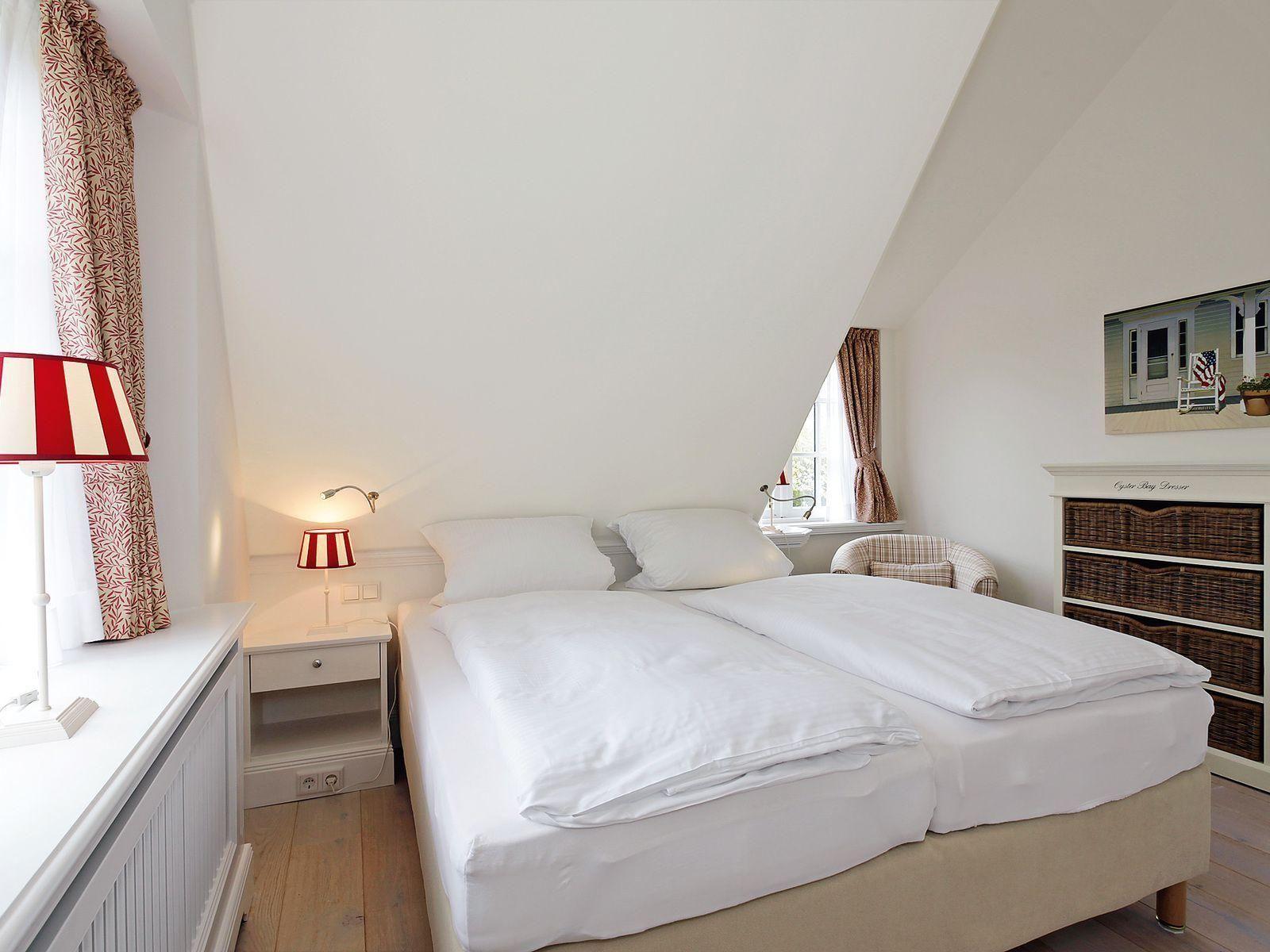 Bedroom with double bed, nightstand, and dresser under sloped ceiling.