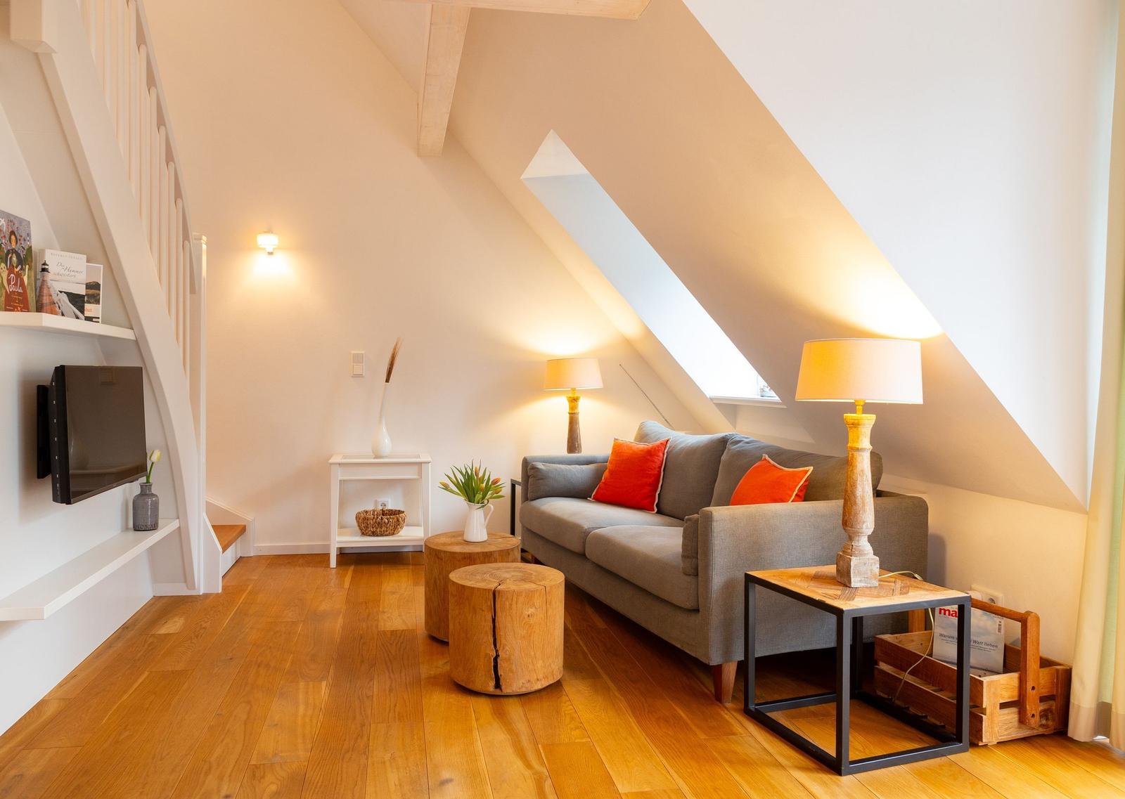 Wohnzimmer mit Sofa, Tischen und Holzboden unter Dachschrägen.