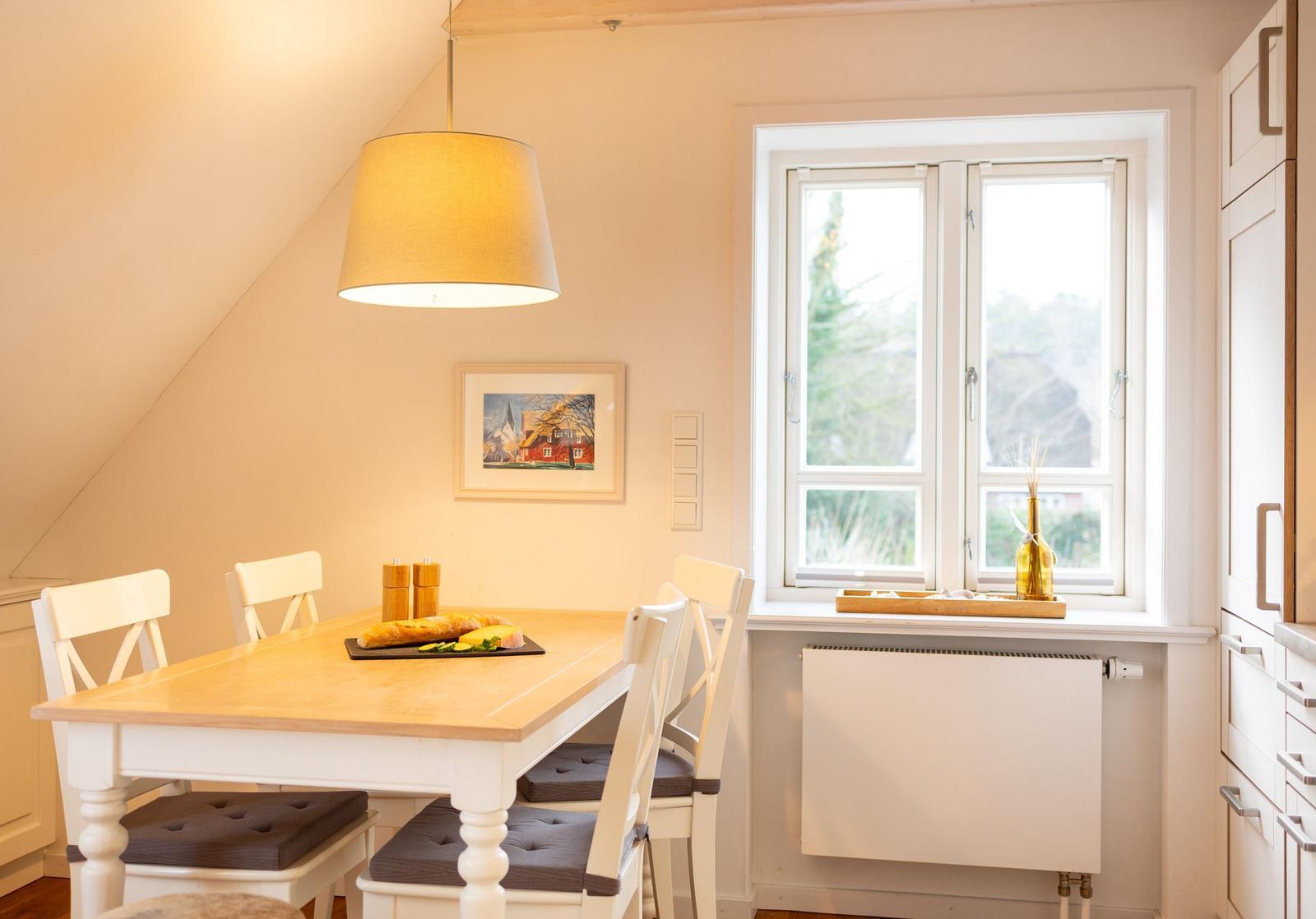 Essbereich mit Tisch, Stühlen und Fenster. Auf dem Tisch steht ein Brötchen.