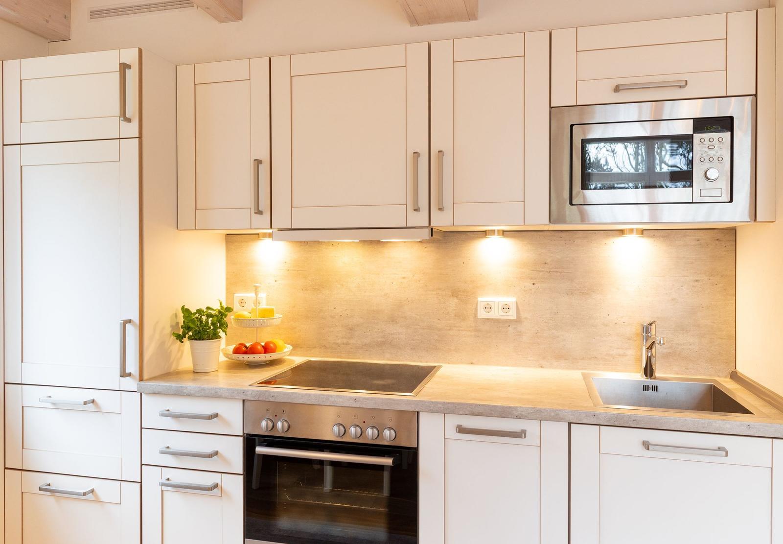 Küche mit weißen Schränken, Herd, Spüle und Mikrowelle.