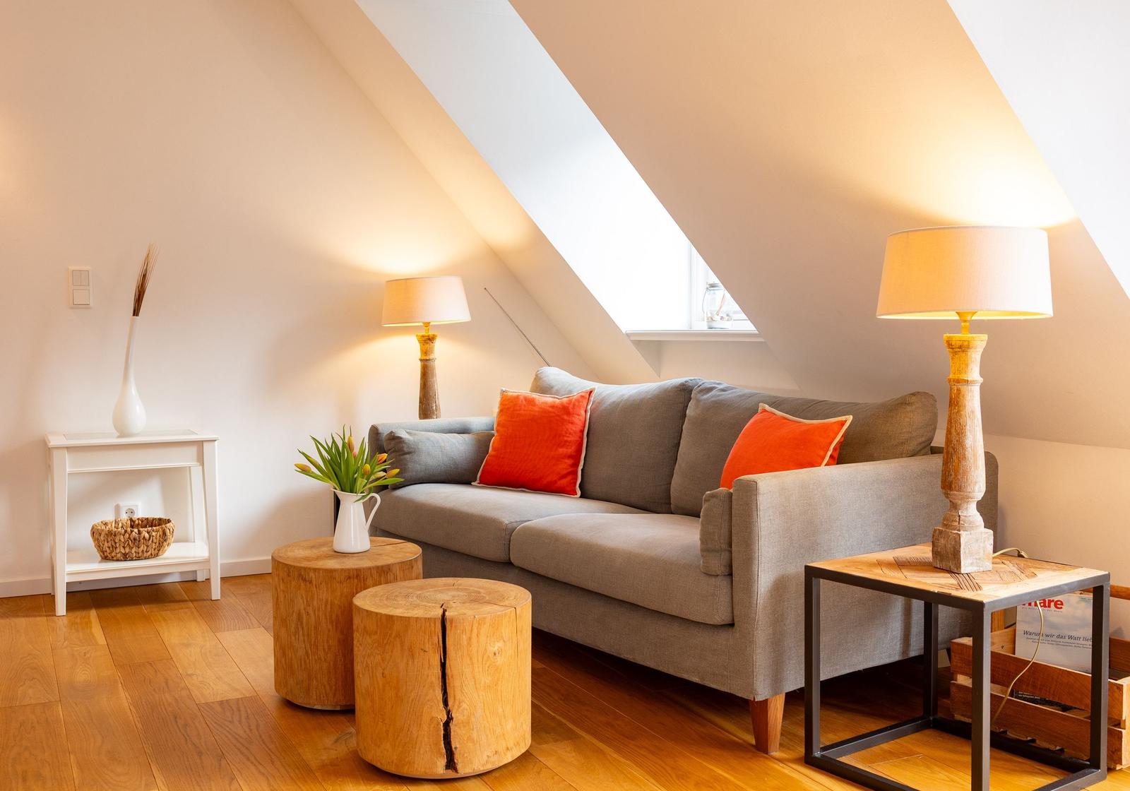 Wohnzimmer mit Sofa, Holztischen und Lampen unter Dachschrägen.