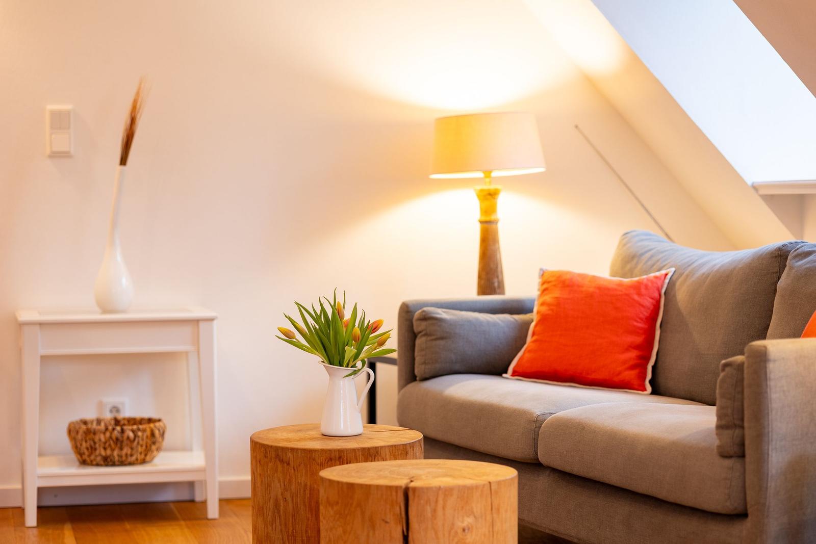 Ein Wohnzimmer mit grauem Sofa, orangefarbenem Kissen, Holztisch und Stehlampe.