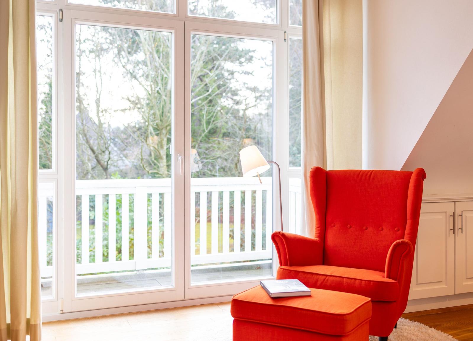 Rotes Sessel mit Fußhocker vor Glasfront zum Balkon