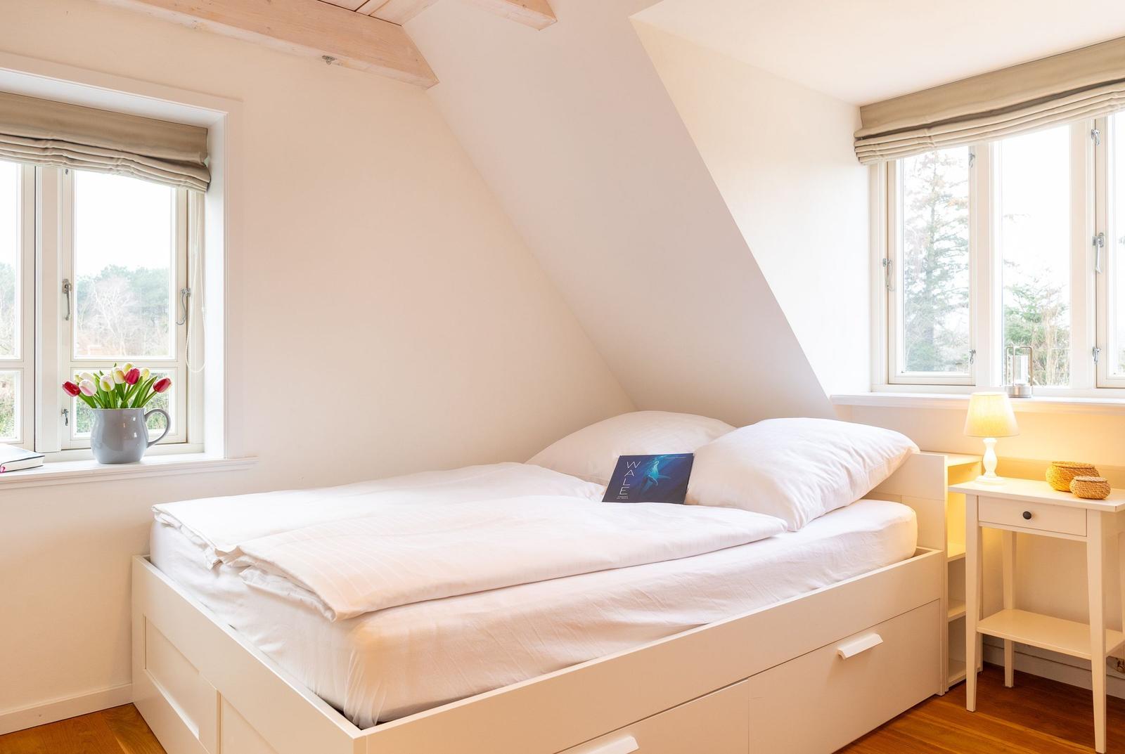 Schlafzimmer mit Dachschrägen, Bett, Nachttisch und Fenstern.