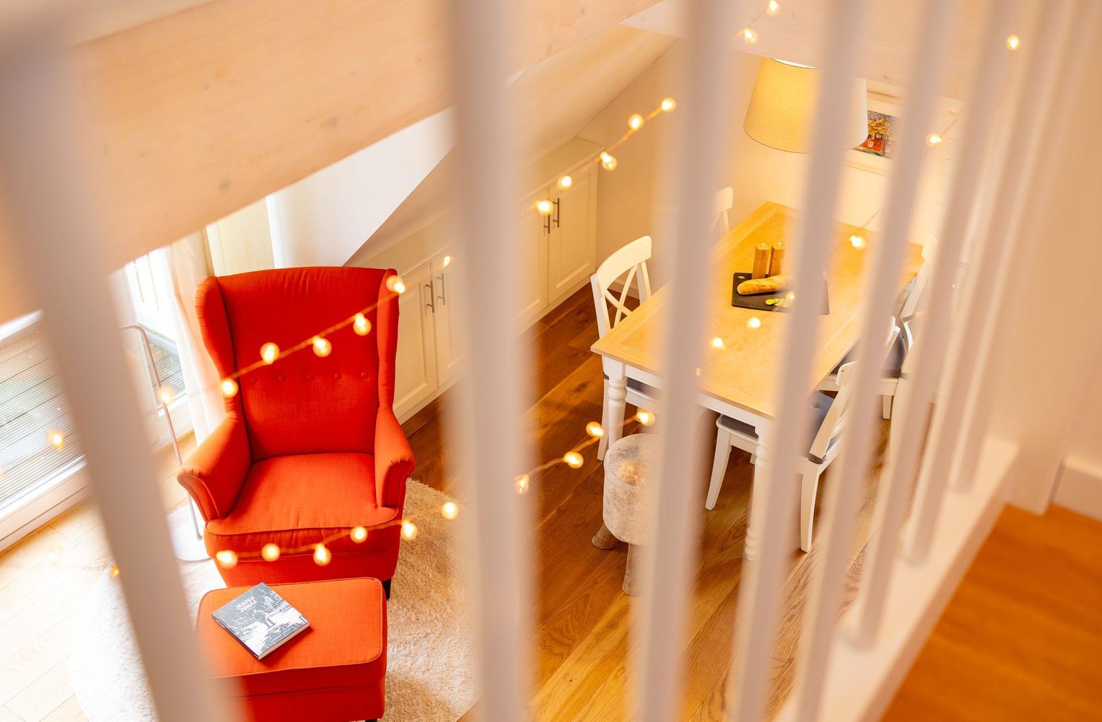 Ein Raum mit rotem Sessel, Esstisch und warmen Lichterketten.